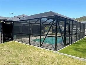Black mesh enclosure around a backyard swimming pool on a sunny lawn