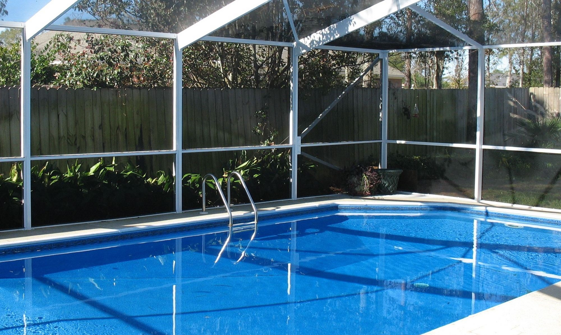 Outdoor swimming pool with bright blue water and white screened enclosure in sunlight