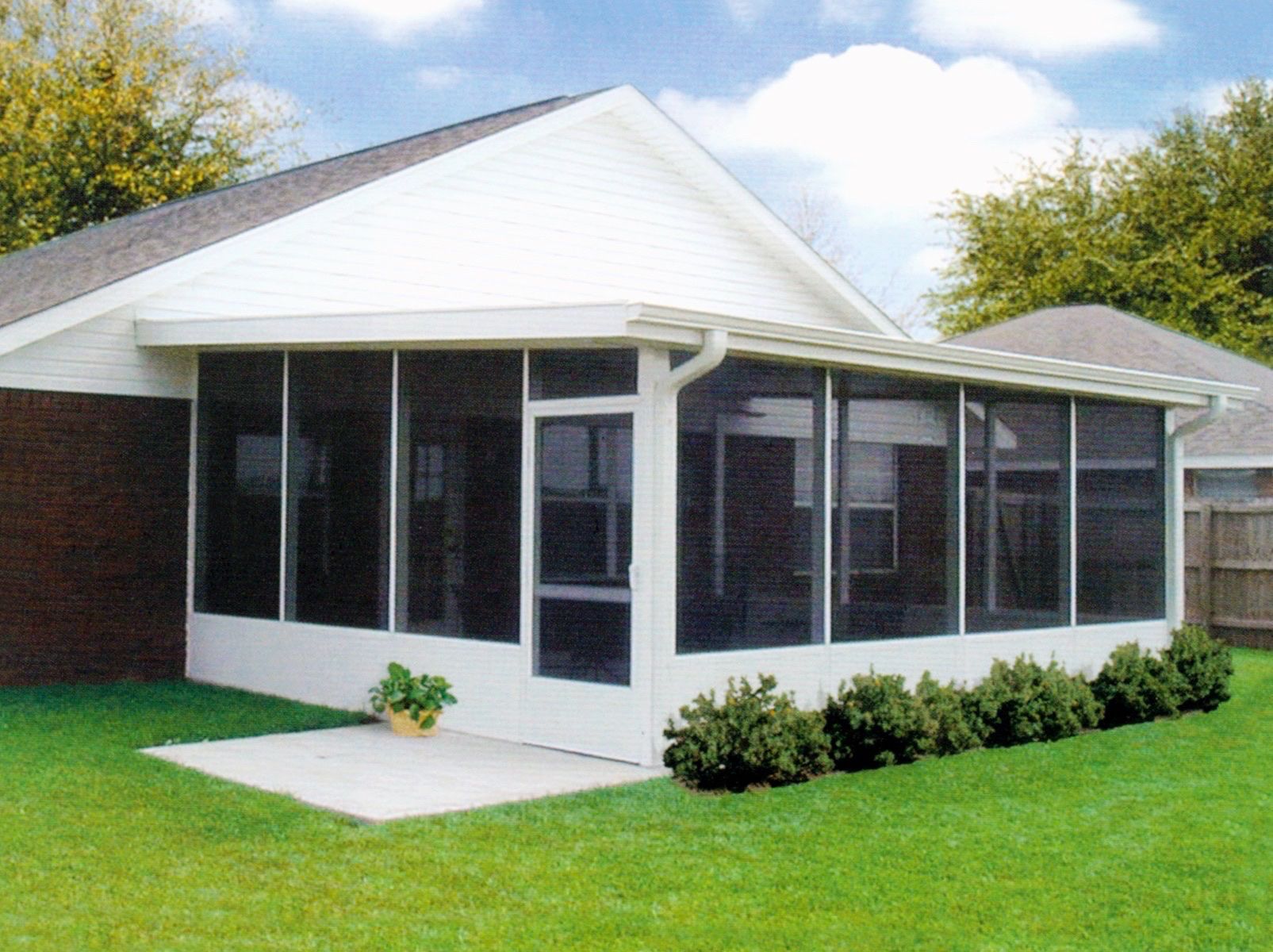Small white house with screened porch, red brick side wall, and green lawn under a blue sky