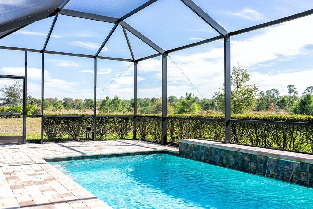 Screened-in backyard pool with blue water, patio tiles, and a view of greenery beyond the enclosure
