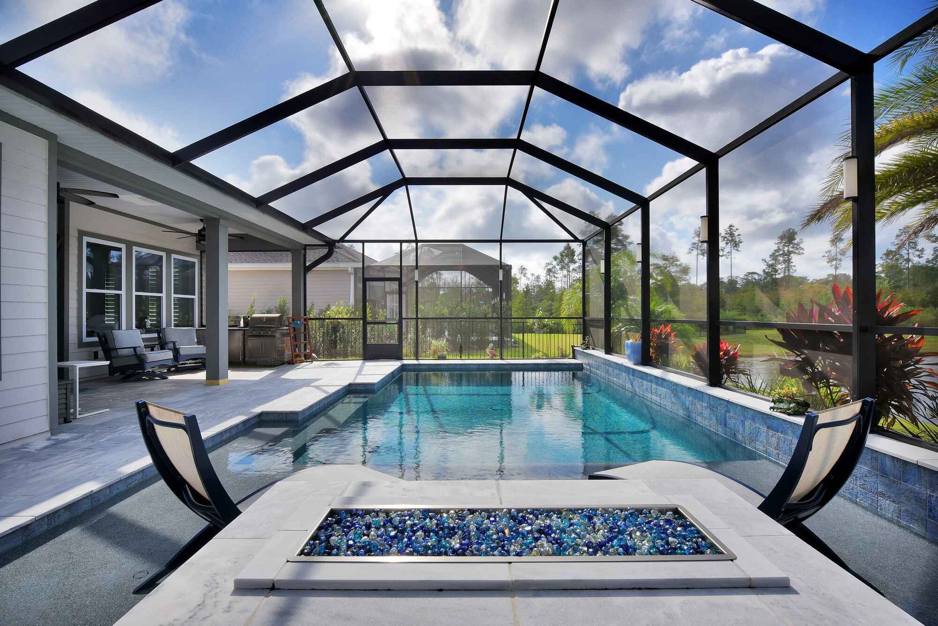 Covered backyard pool with hot tub, black screen enclosure, and modern patio beside a house