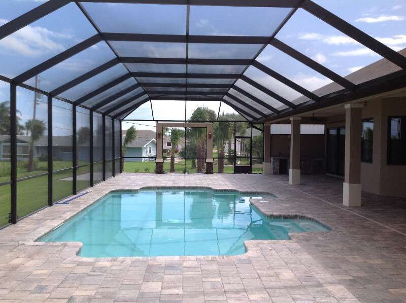 Covered outdoor swimming pool with a screened enclosure, tiled deck, and patio beside a house.