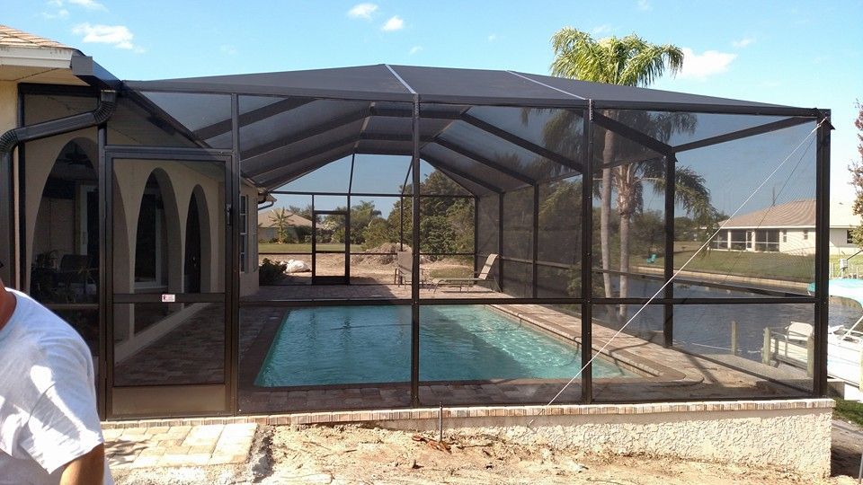 Screened backyard pool enclosure beside a stucco house under a sunny sky