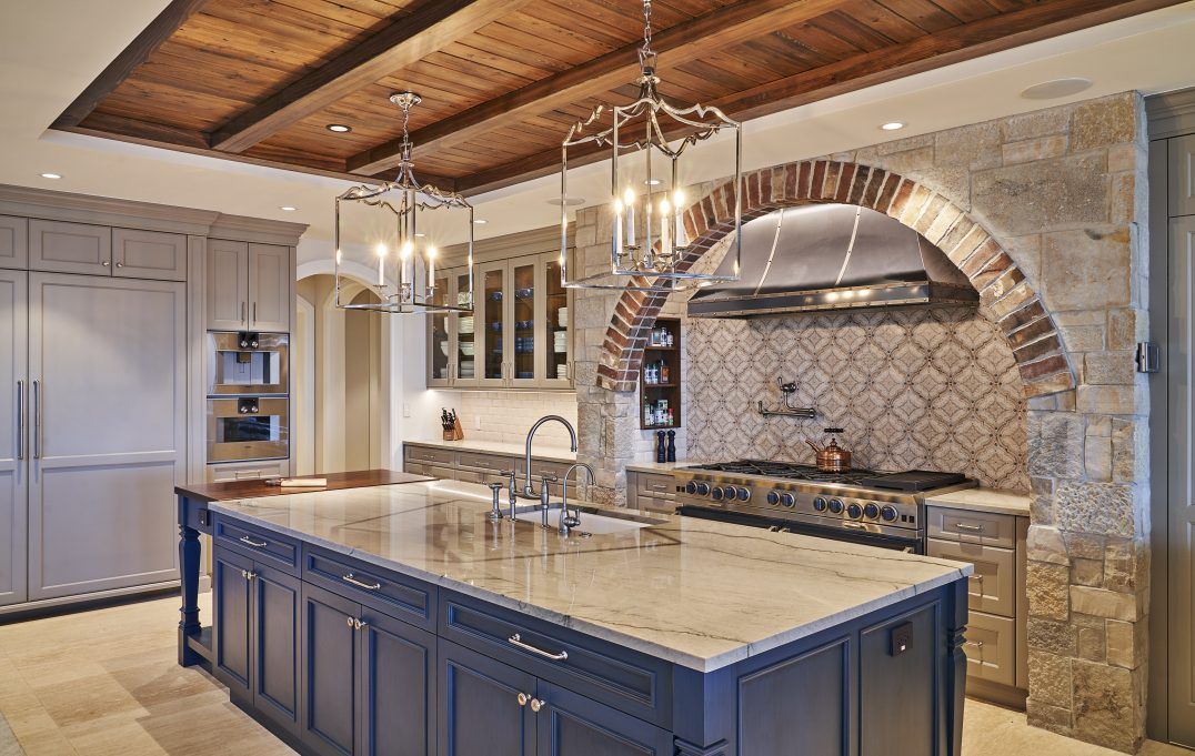 Elegant kitchen with blue island, stone arch, wood ceiling, and chandeliers