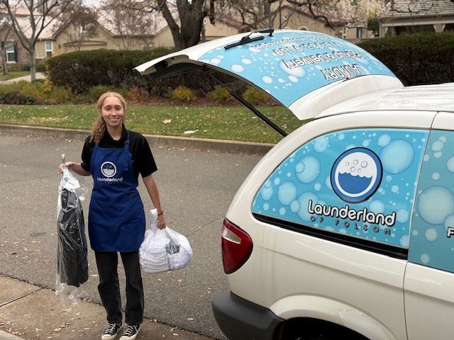 Woman in apron holding laundry bags by a van with laundry service branding.
