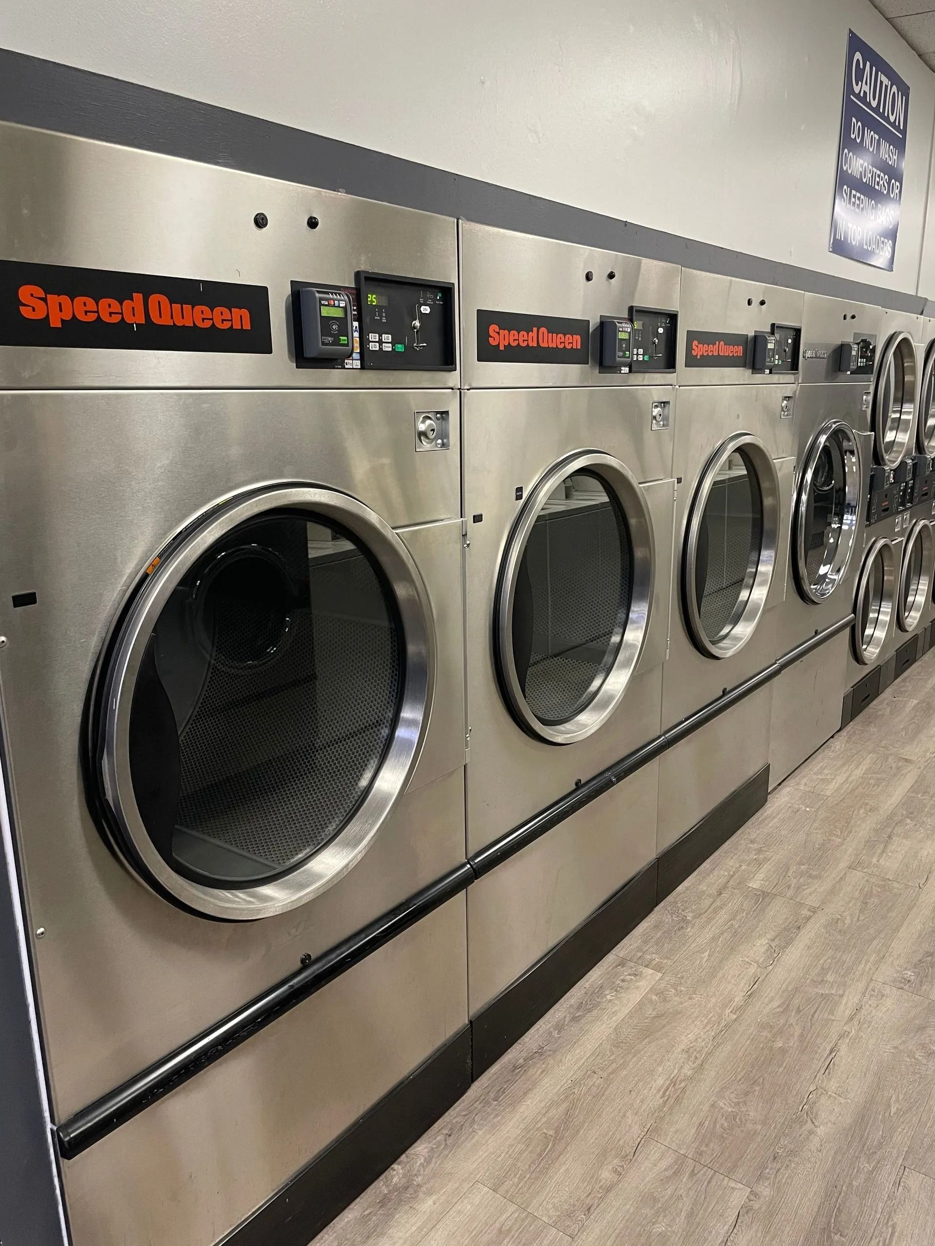 Row of Speed Queen commercial washing machines in a laundromat, stainless steel with black trim.