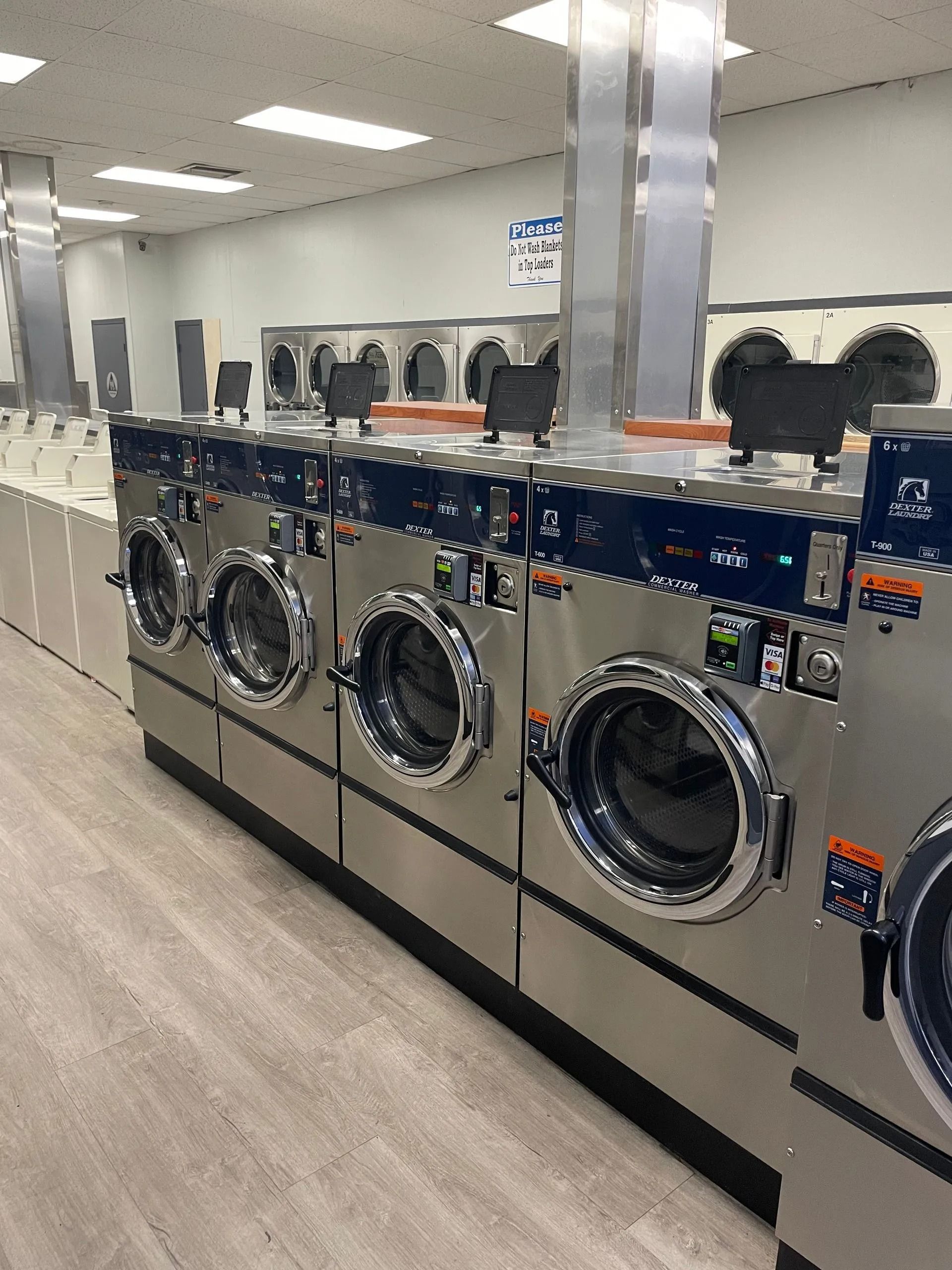 Row of commercial washing machines in a laundromat, stainless steel with blue accents.