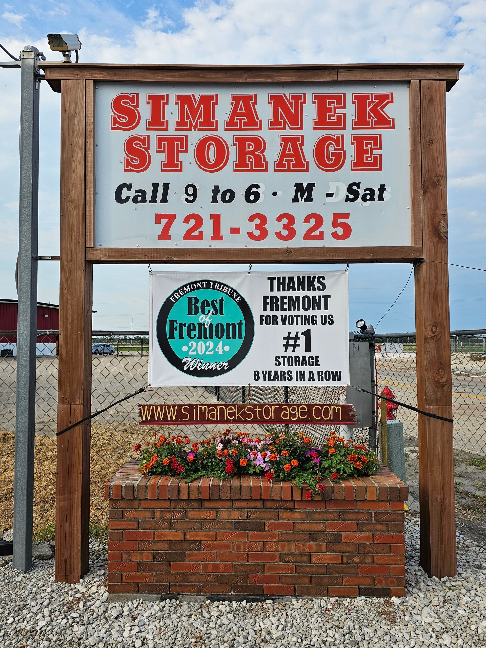 A sign for Simanek Storage with flowers in front of it