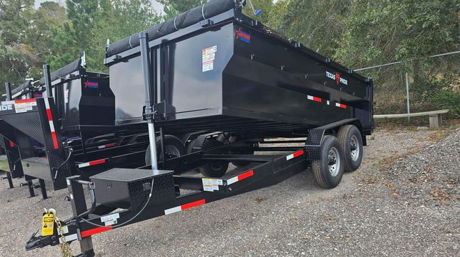 Black dump trailer with tarp cover parked on a gravel lot outdoors