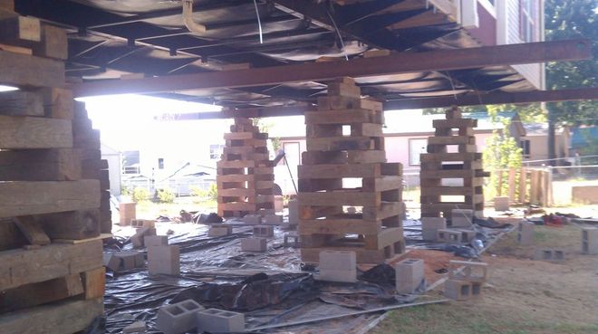 Shelter-like structure on stacked wooden supports, with debris and sunlight streaming through the open area underneath.