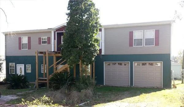 Two-story house with teal lower siding, red shutters, front porch, and double garage doors