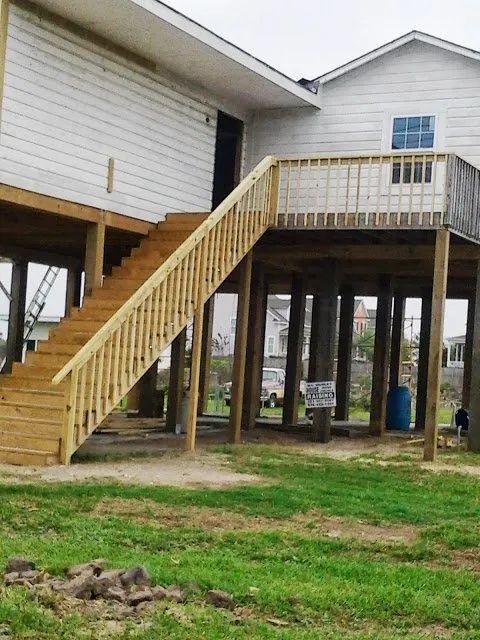 Elevated house with wooden exterior stairs and deck over a grassy yard
