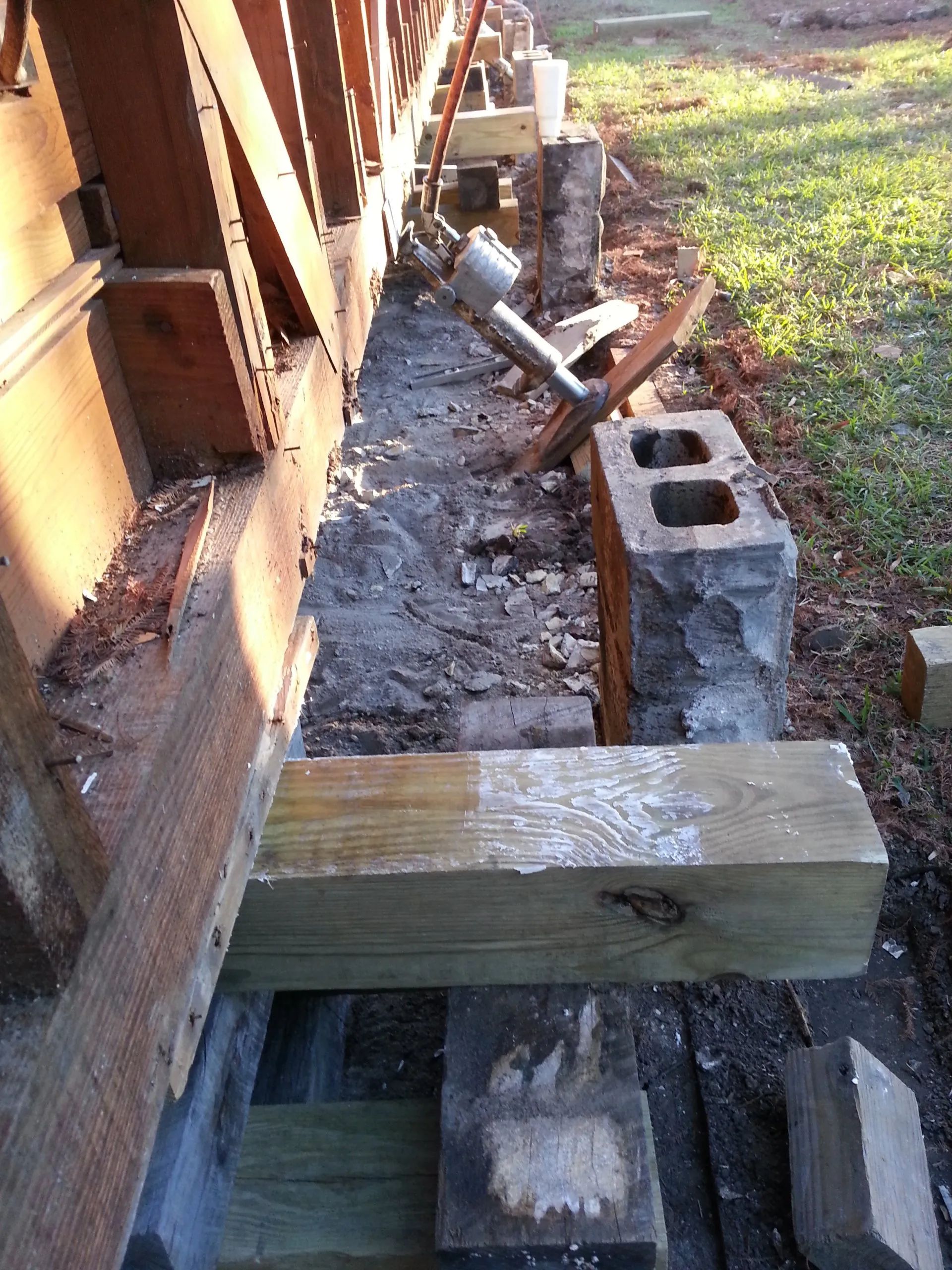 Construction site beside house foundation with wooden supports, cinder blocks, and wet concrete trench