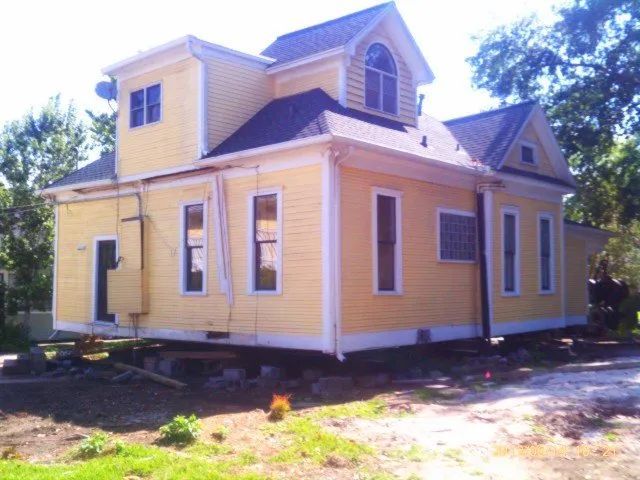Yellow house on blocks with white trim and a small porch, shown outdoors in daylight.
