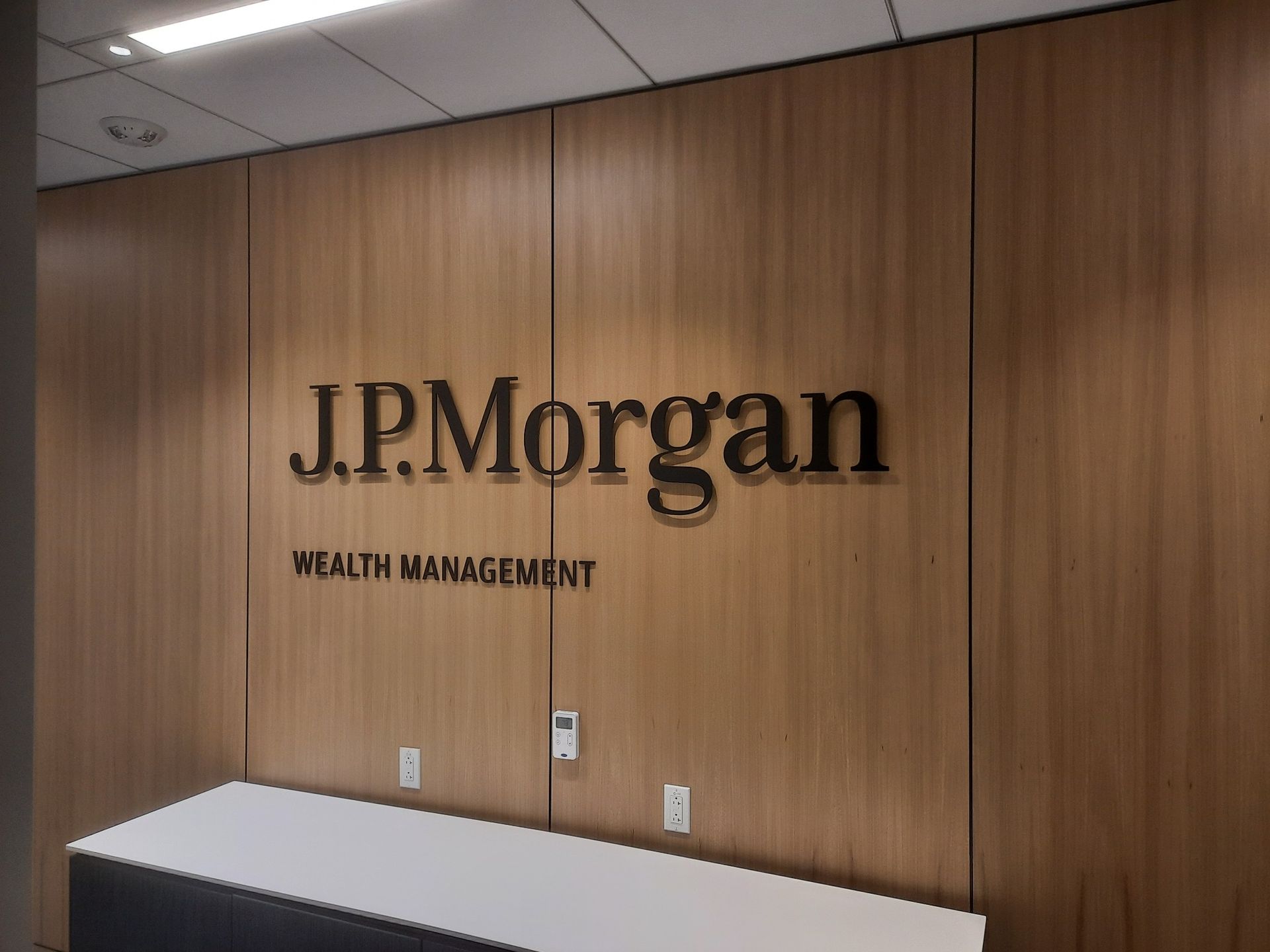 J.P. Morgan Wealth Management sign on a wood-paneled office wall with a white reception desk below