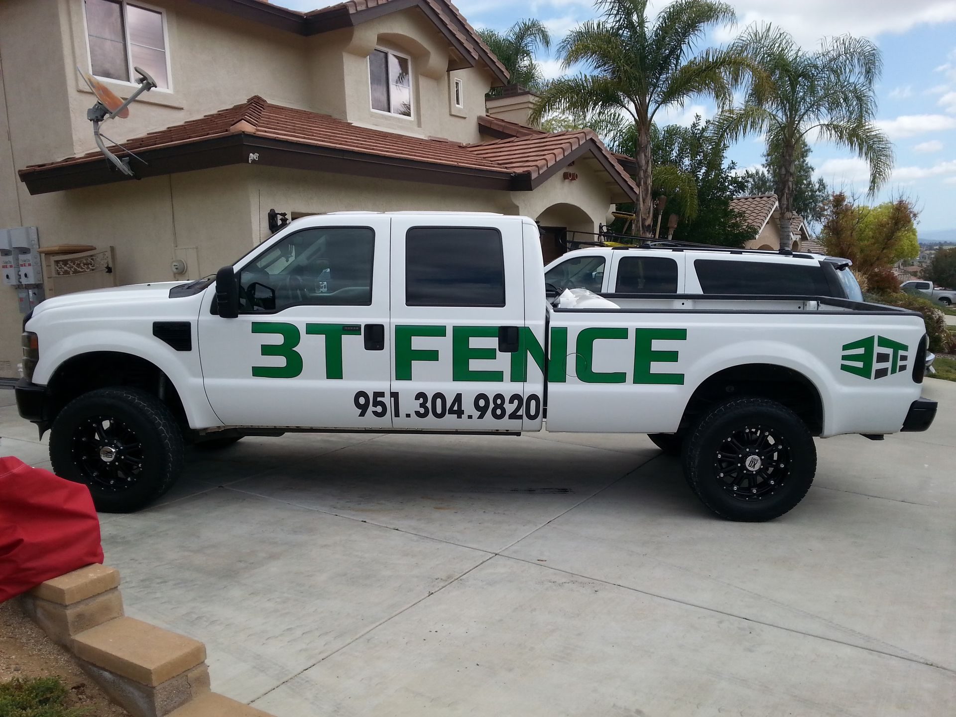 White 3T Fence pickup truck parked in a driveway in front of a house, with company logo and phone number.