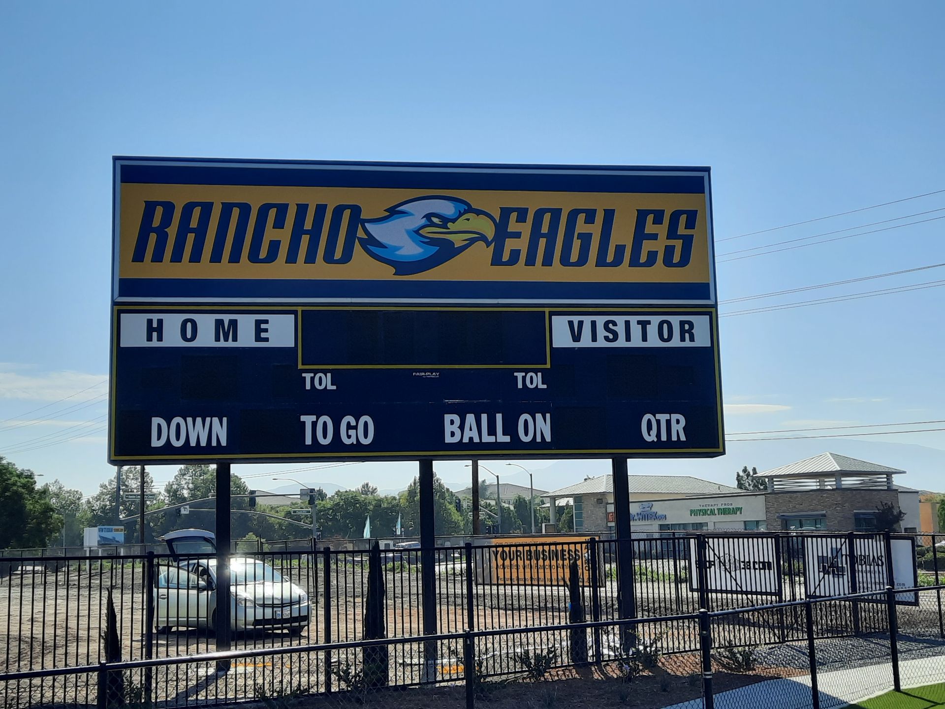 Rancho Eagles scoreboard at a football field with blue sky and chain-link fence nearby