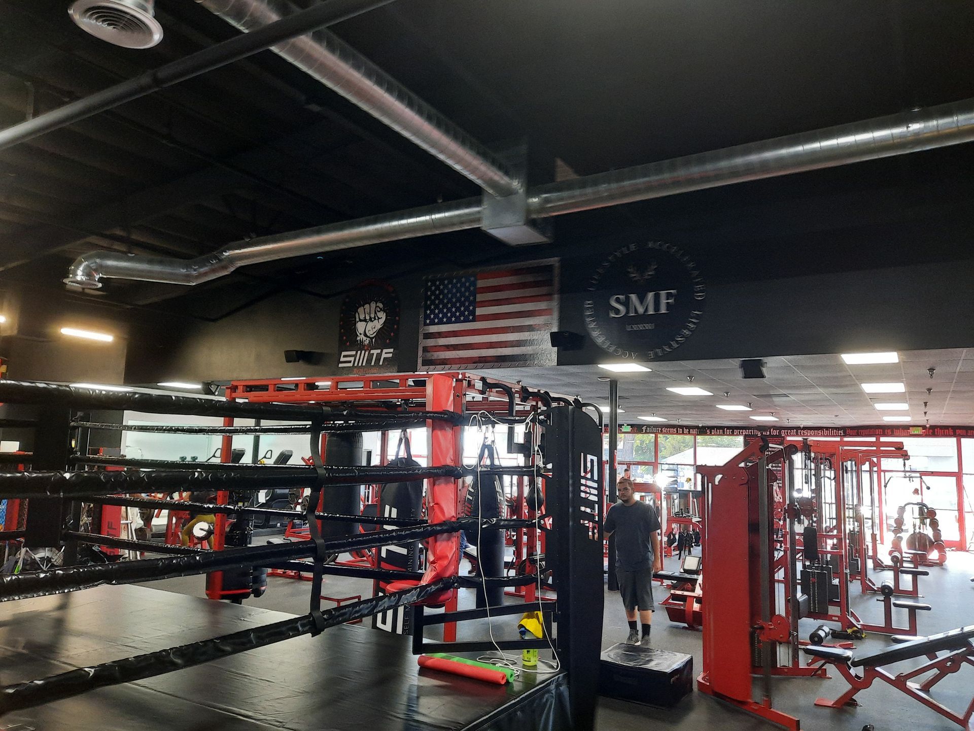 Indoor boxing gym with red ring ropes, heavy bags, and workout equipment under bright lights