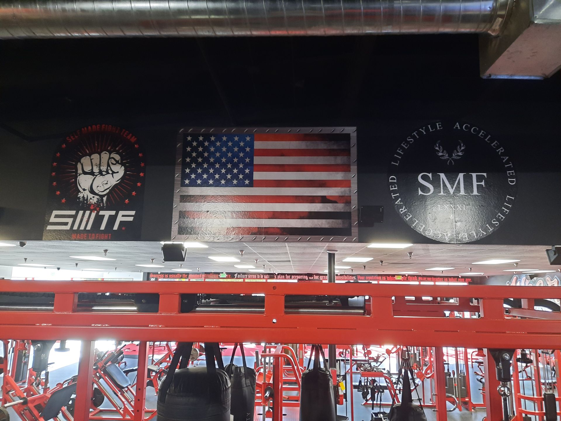 Gym wall with SWIFT logo, American flag, and SMF emblem above red exercise equipment