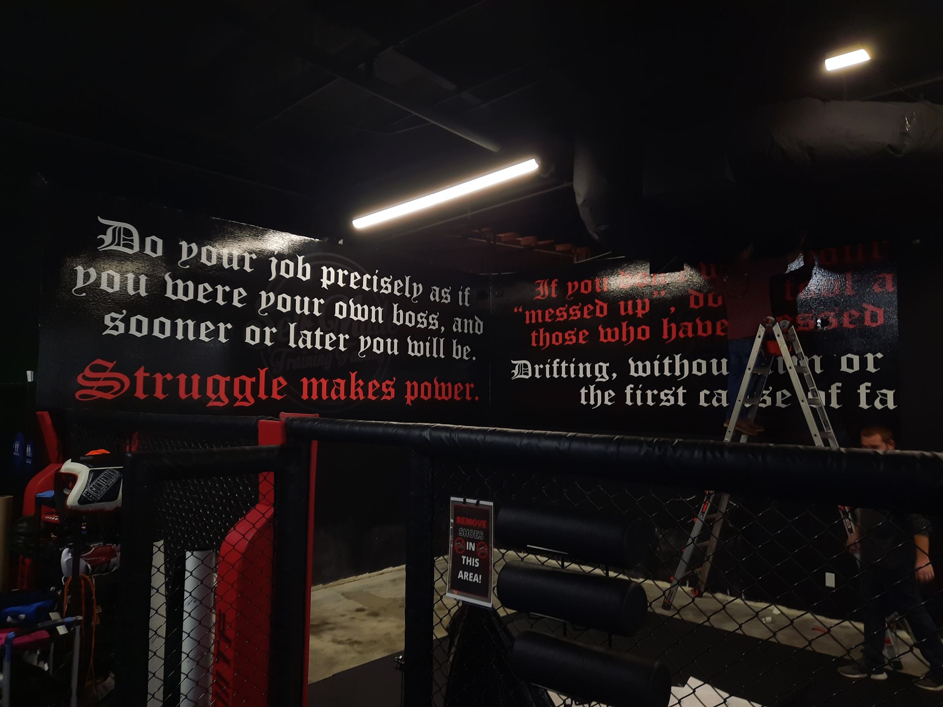 Dim wrestling-themed wall mural with red and white quotes in a dark room, lit by ceiling lights.