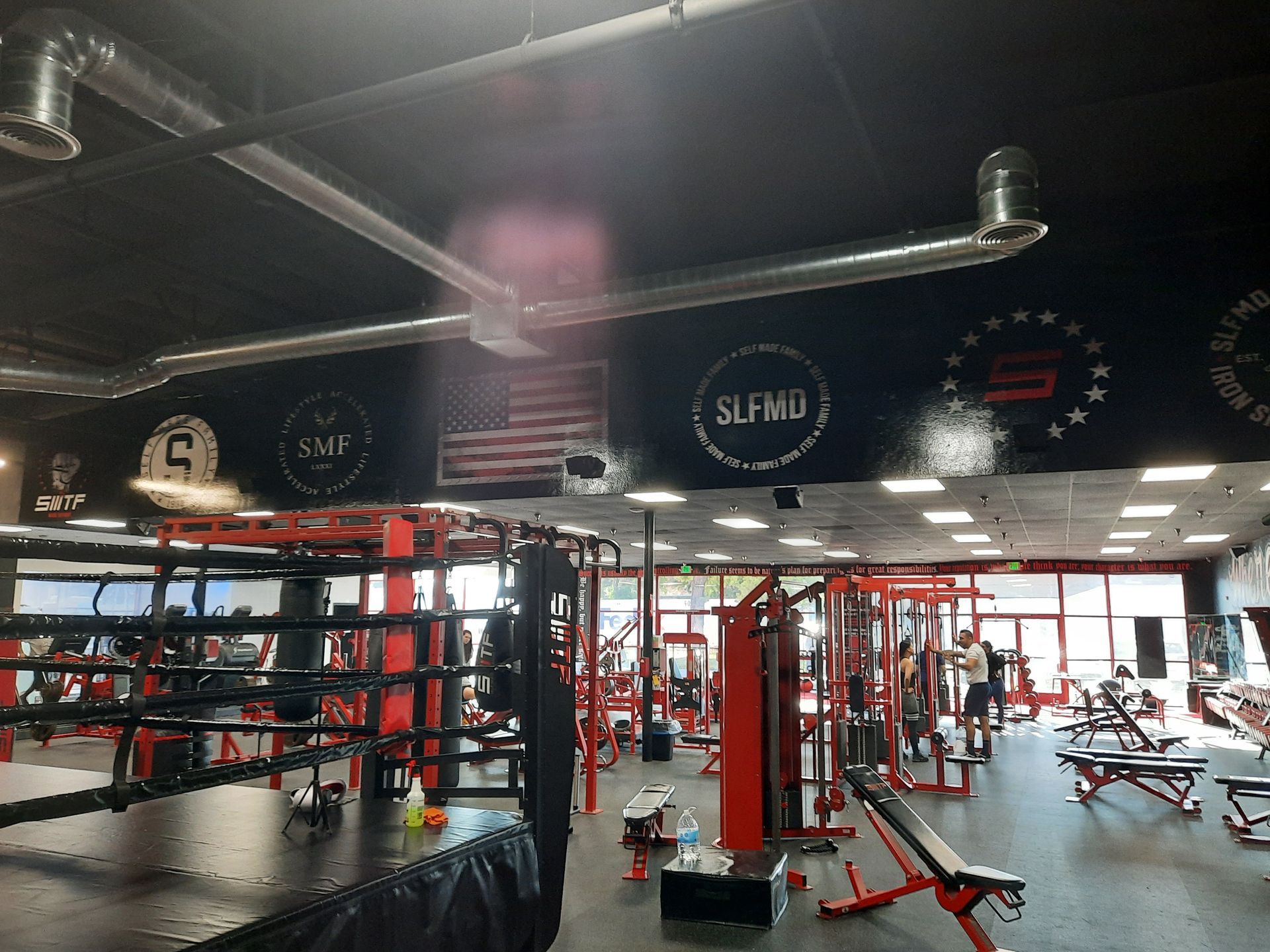 Spacious boxing gym with red-and-black equipment, ring, punching bags, and overhead lights
