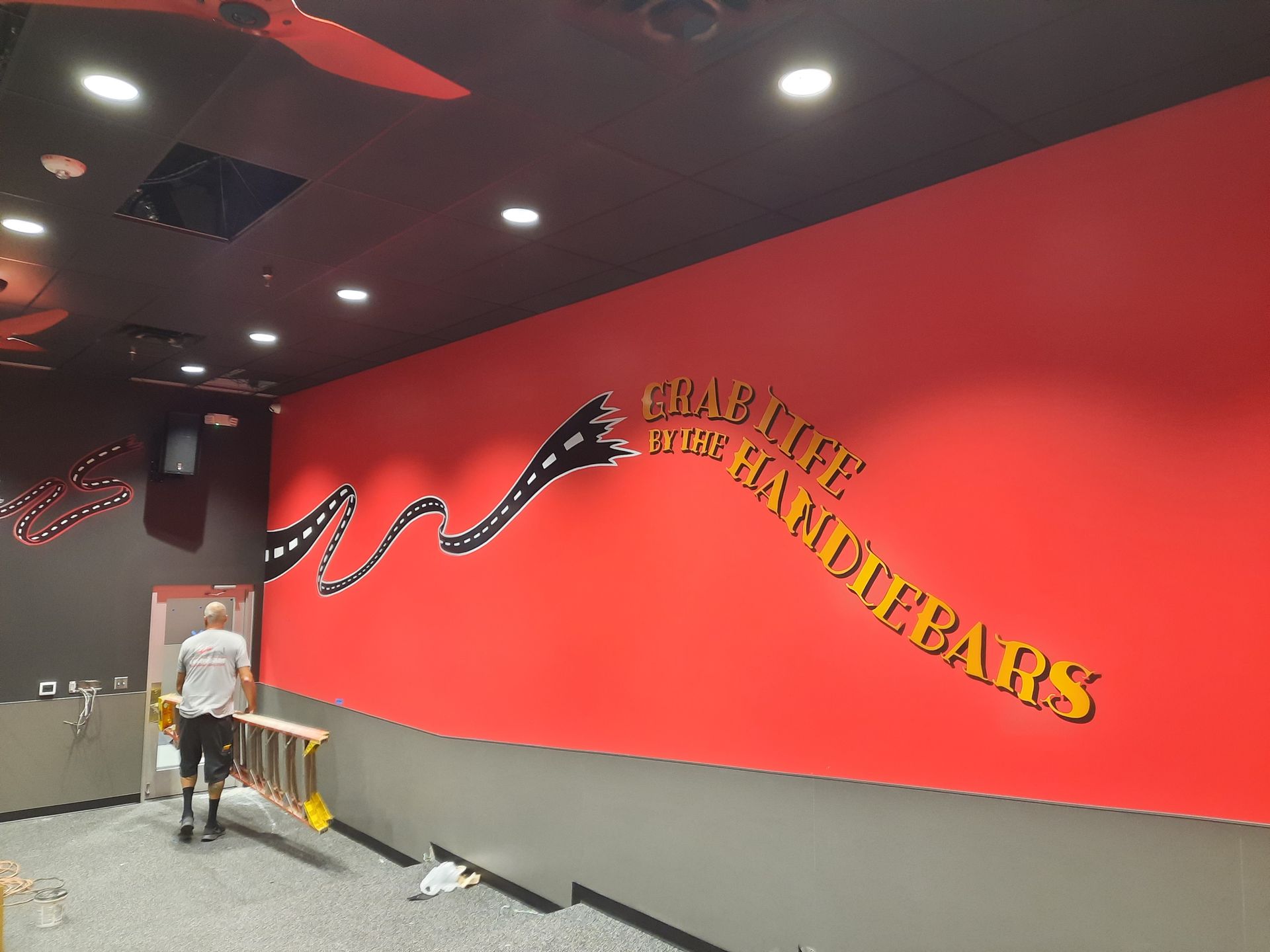 Indoor climbing gym with red wall mural and a person walking along the corridor