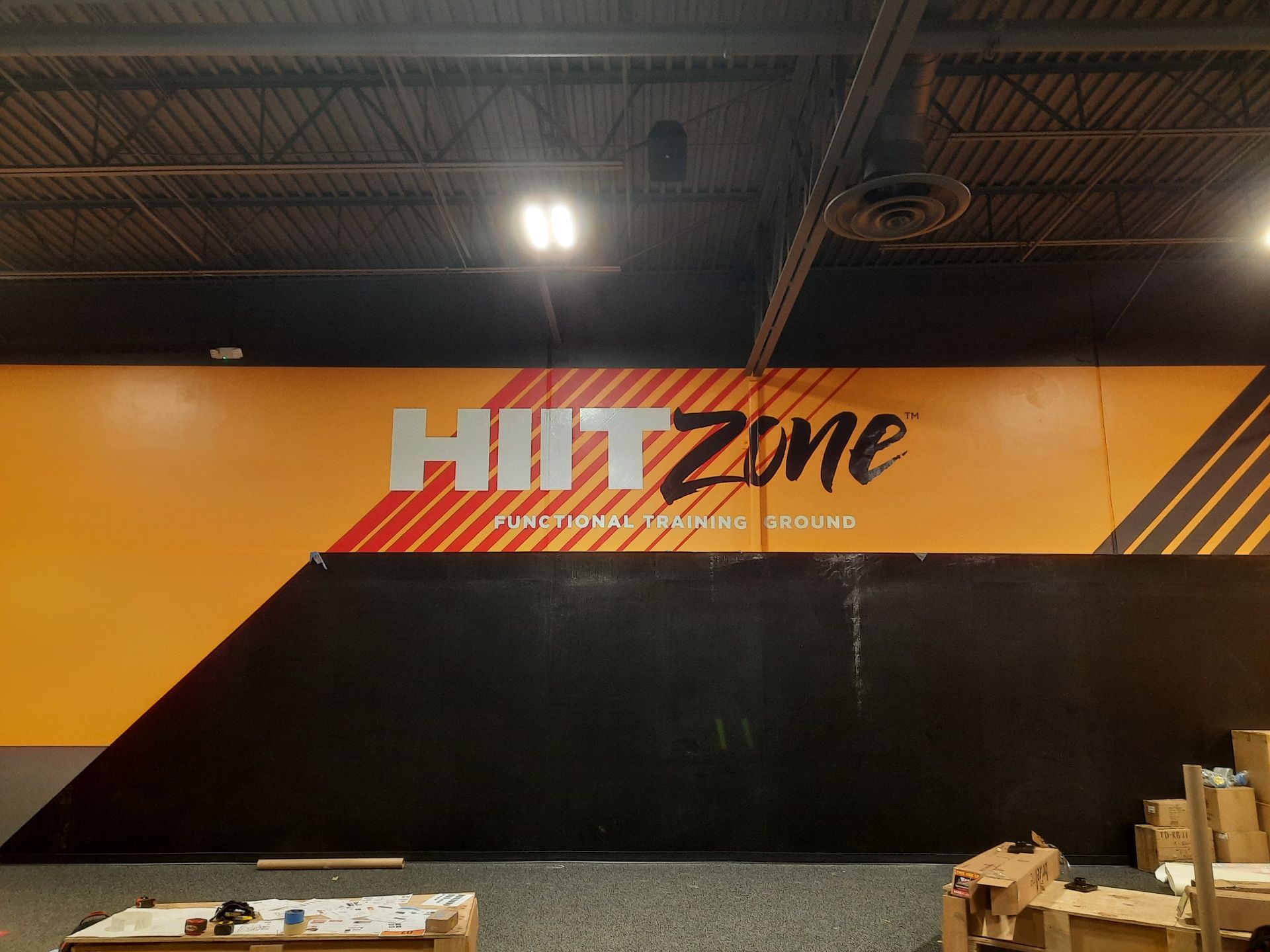 HIT Zone wall logo in an indoor gym with orange, black, and gray walls and high ceiling lights