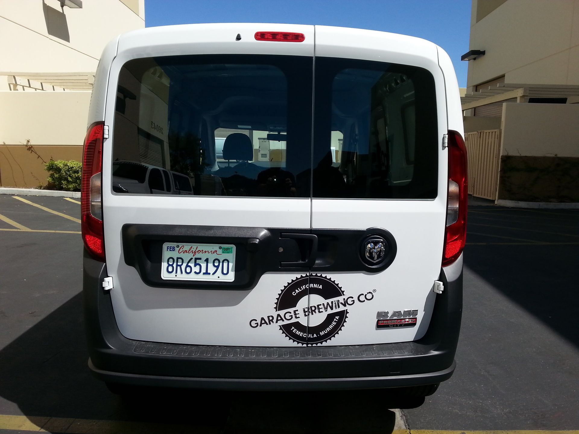 White cargo van viewed from behind, parked outdoors with company logo and California license plate visible