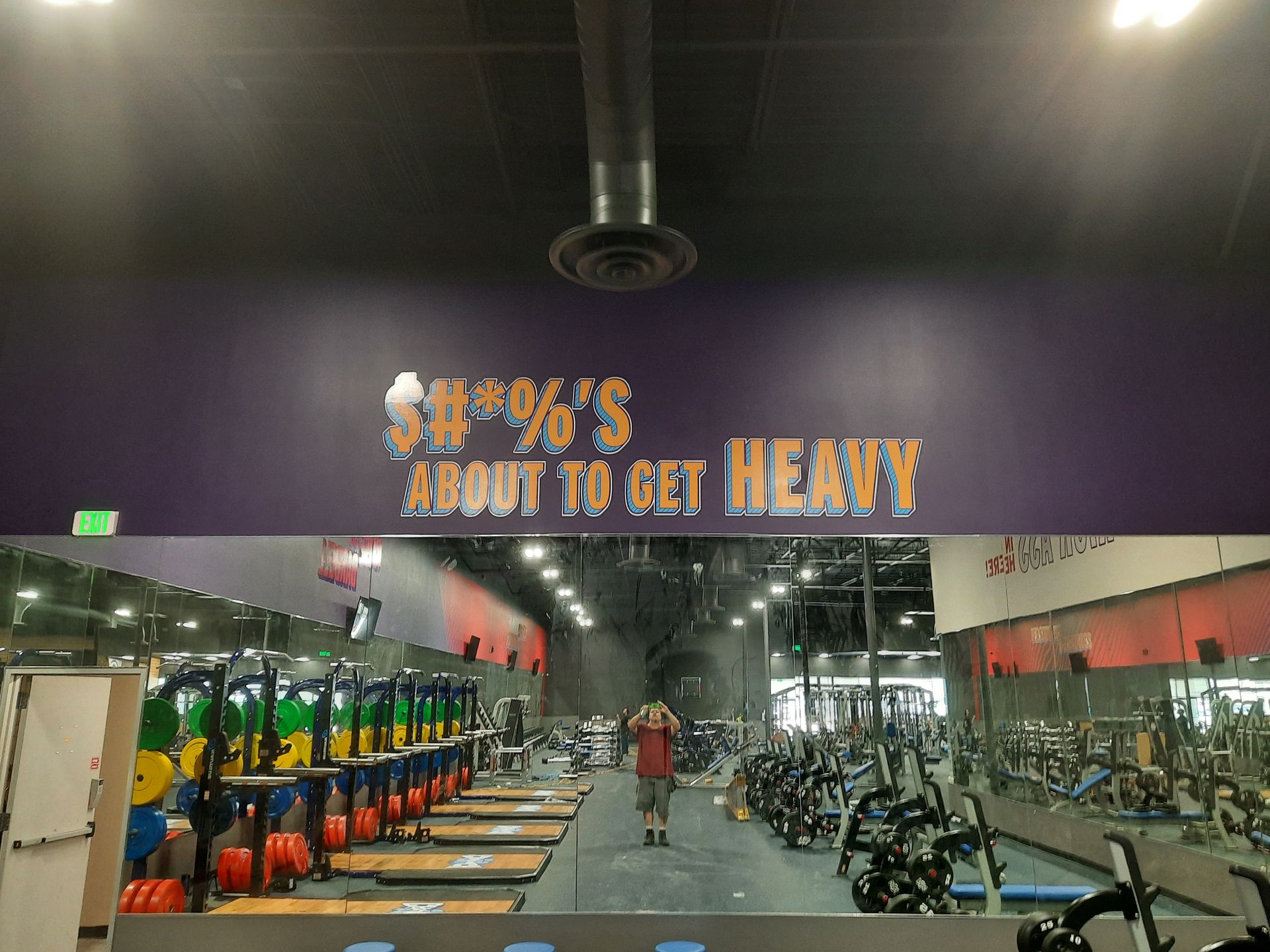 Fitness gym interior with weight racks, dumbbells, exercise machines, and a wall sign reading “HOW TO GET HEALTHY”