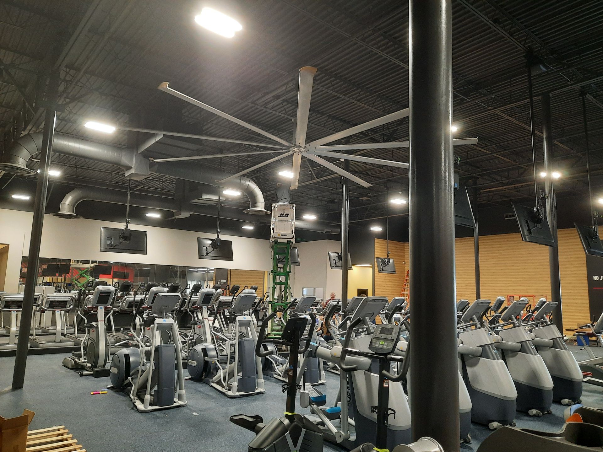 Large gym interior with rows of exercise bikes and treadmills under bright overhead lights.