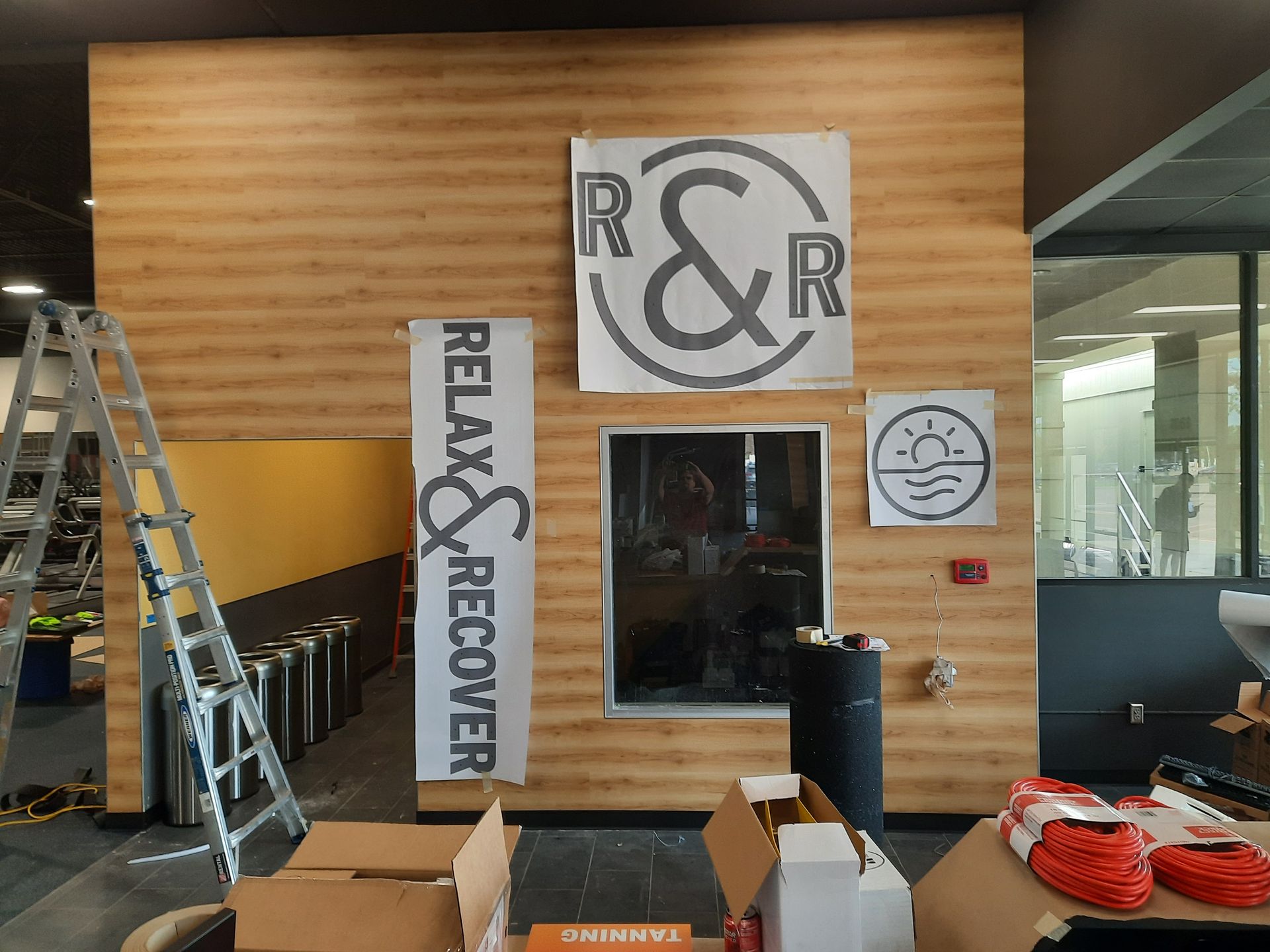 Interior of a new café with wooden wall signage, ladders, cardboard boxes, and a counter under construction