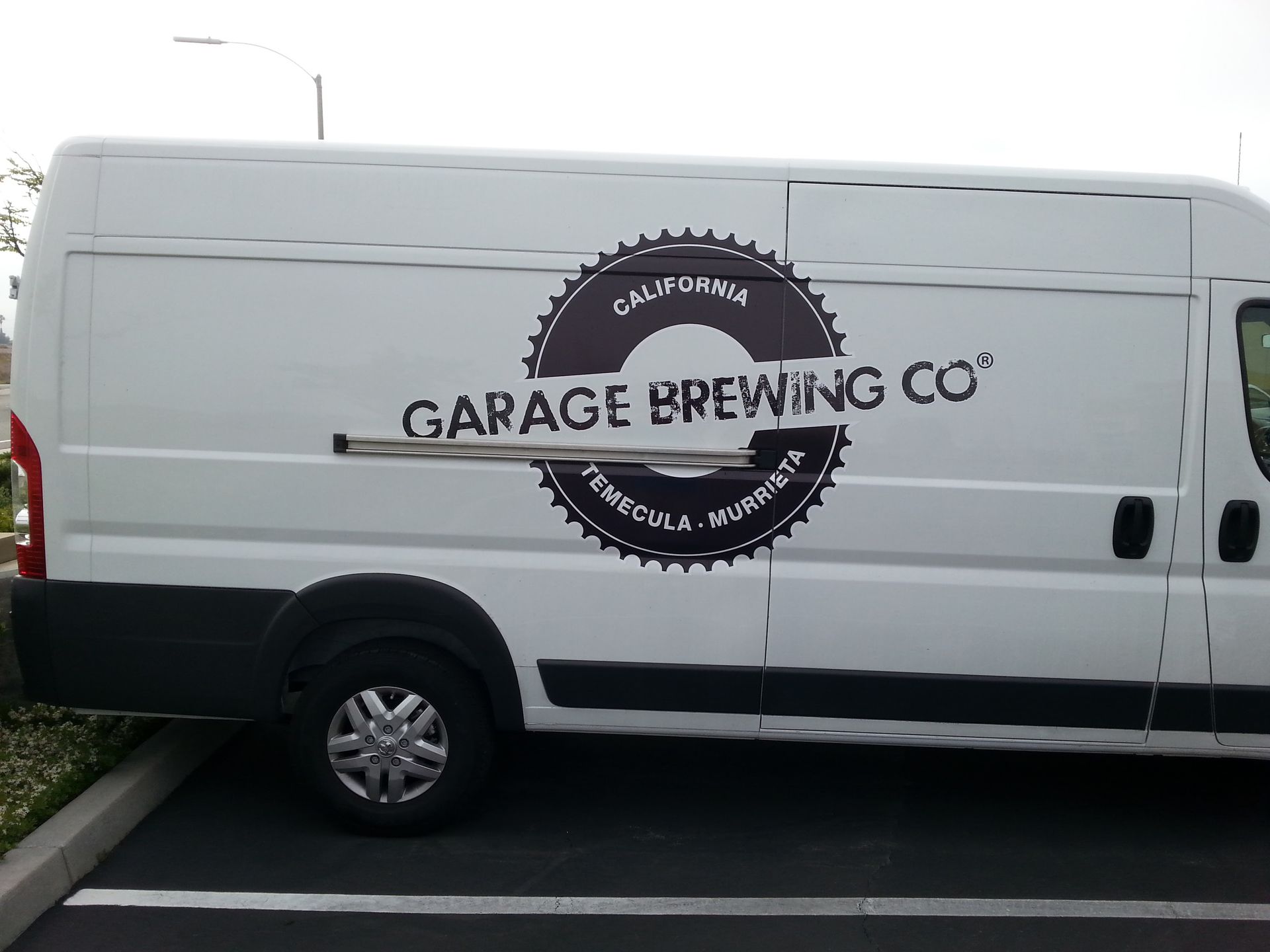 White Garage Brewing Co. van parked outdoors beside a curb and building