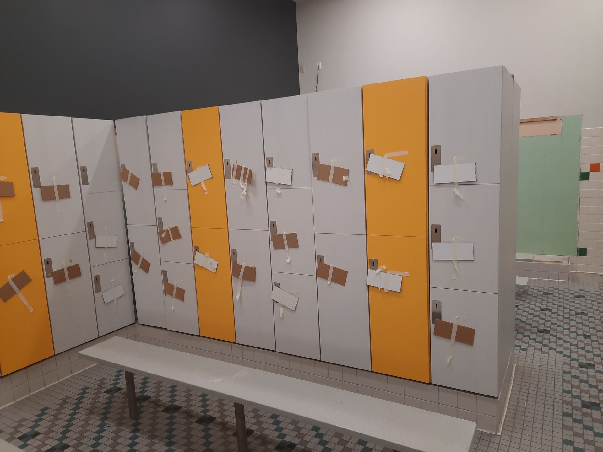 Row of white and orange restroom/locker stalls with paper signs in a tiled room