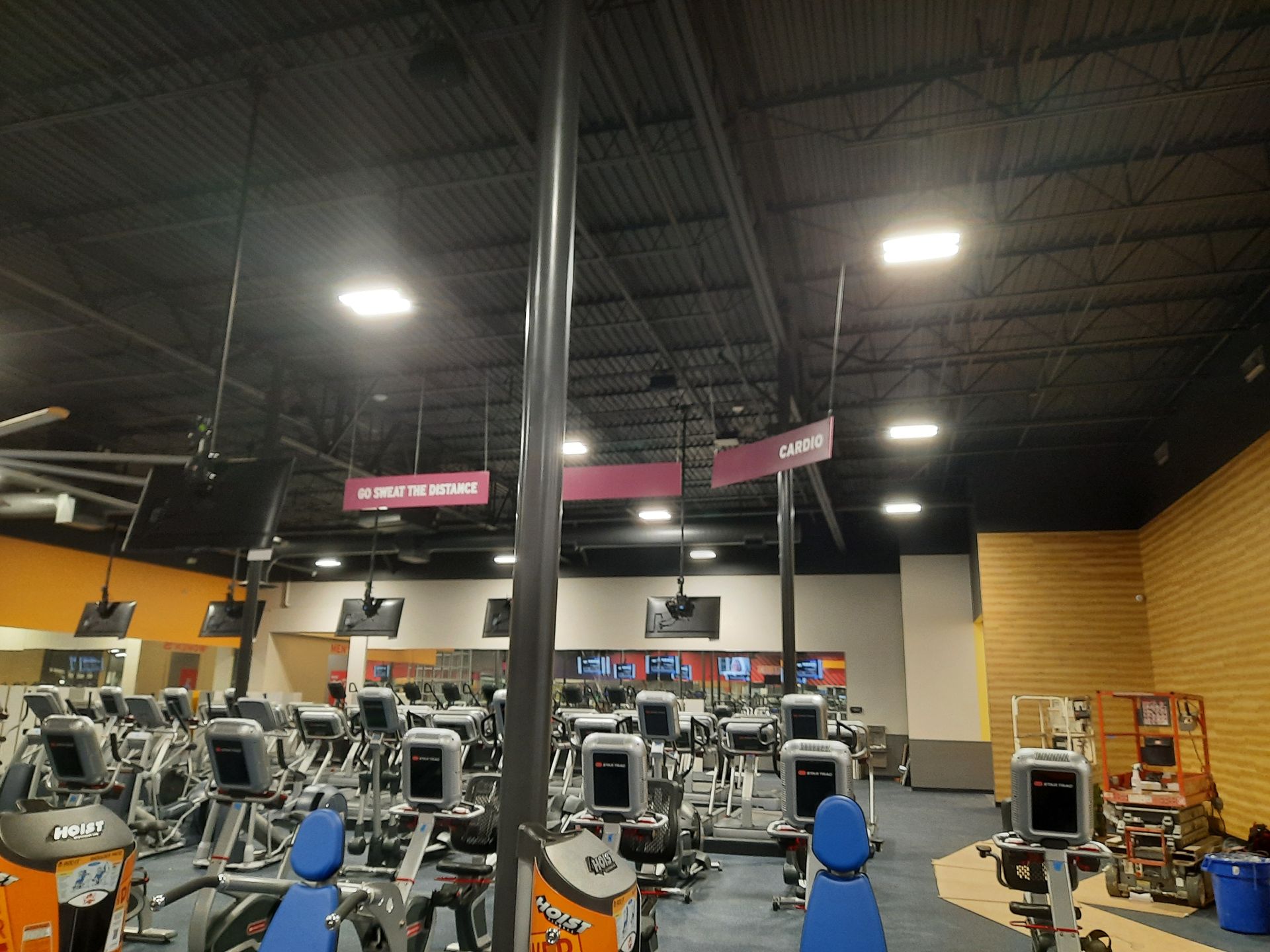 Indoor gym with rows of exercise machines and high industrial ceiling lights