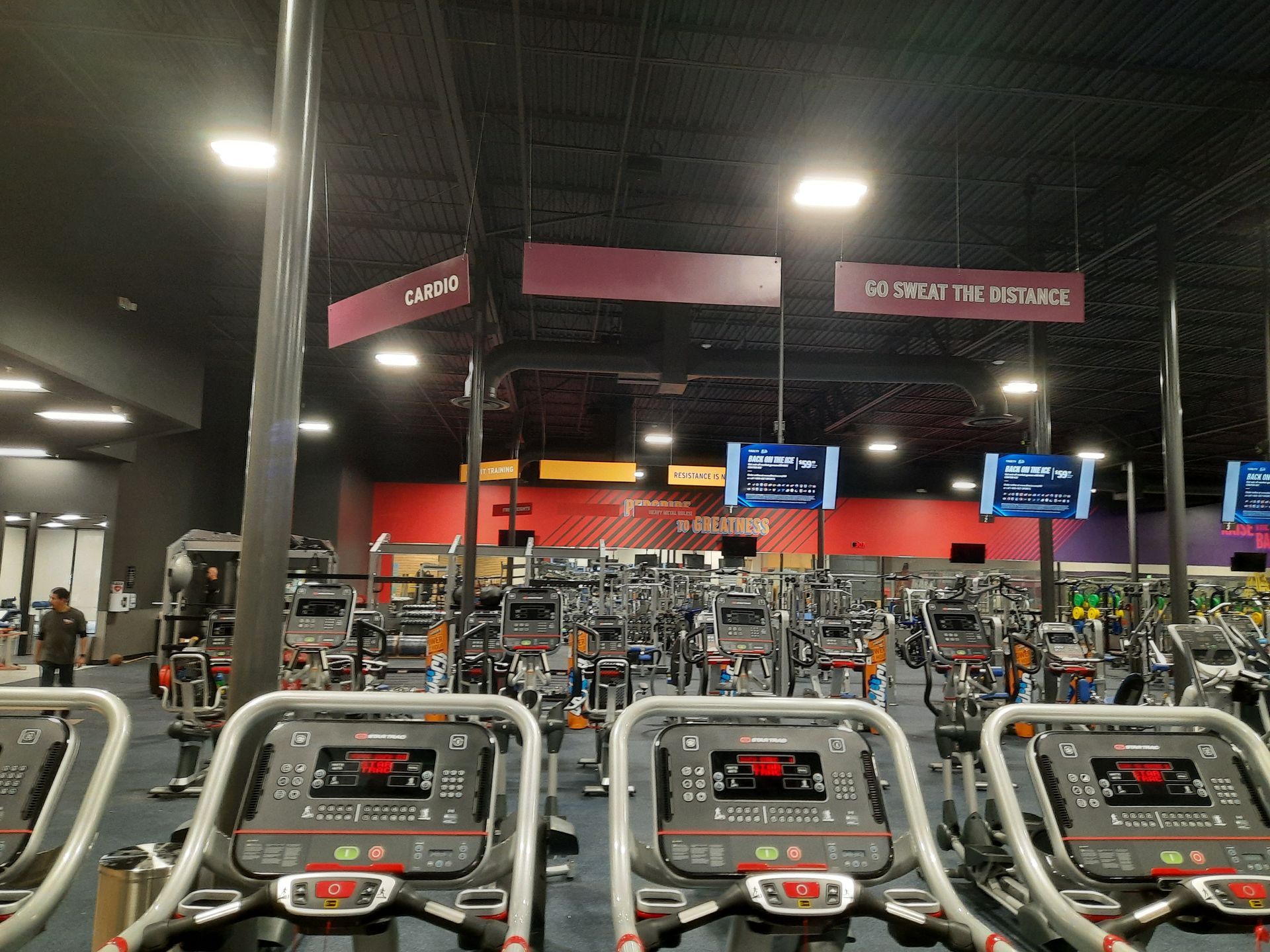 Rows of treadmills in a dimly lit gym with red accents and TV screens overhead