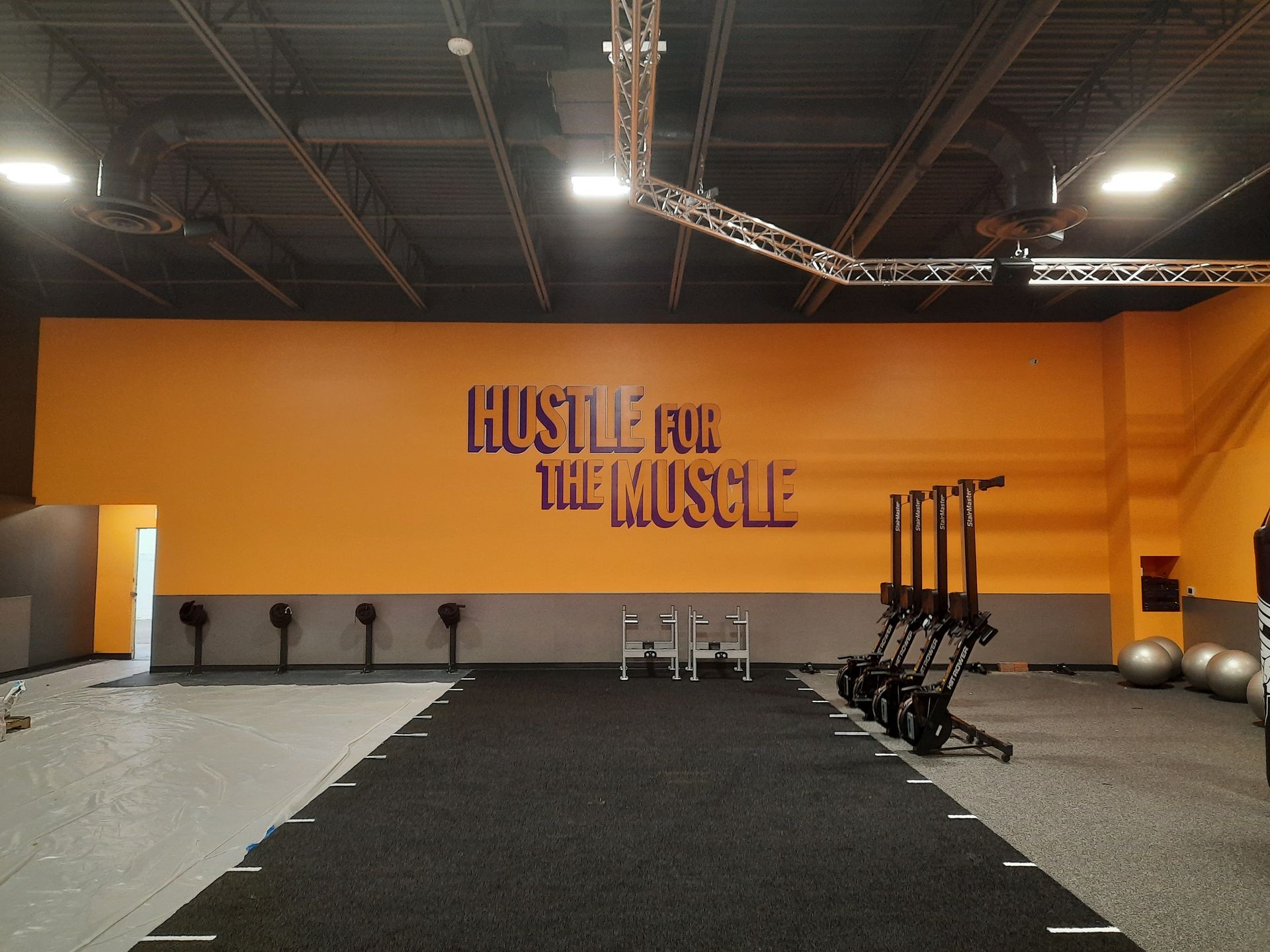Empty gym with orange wall reading “Hustle for the Hustle” and black turf lane.