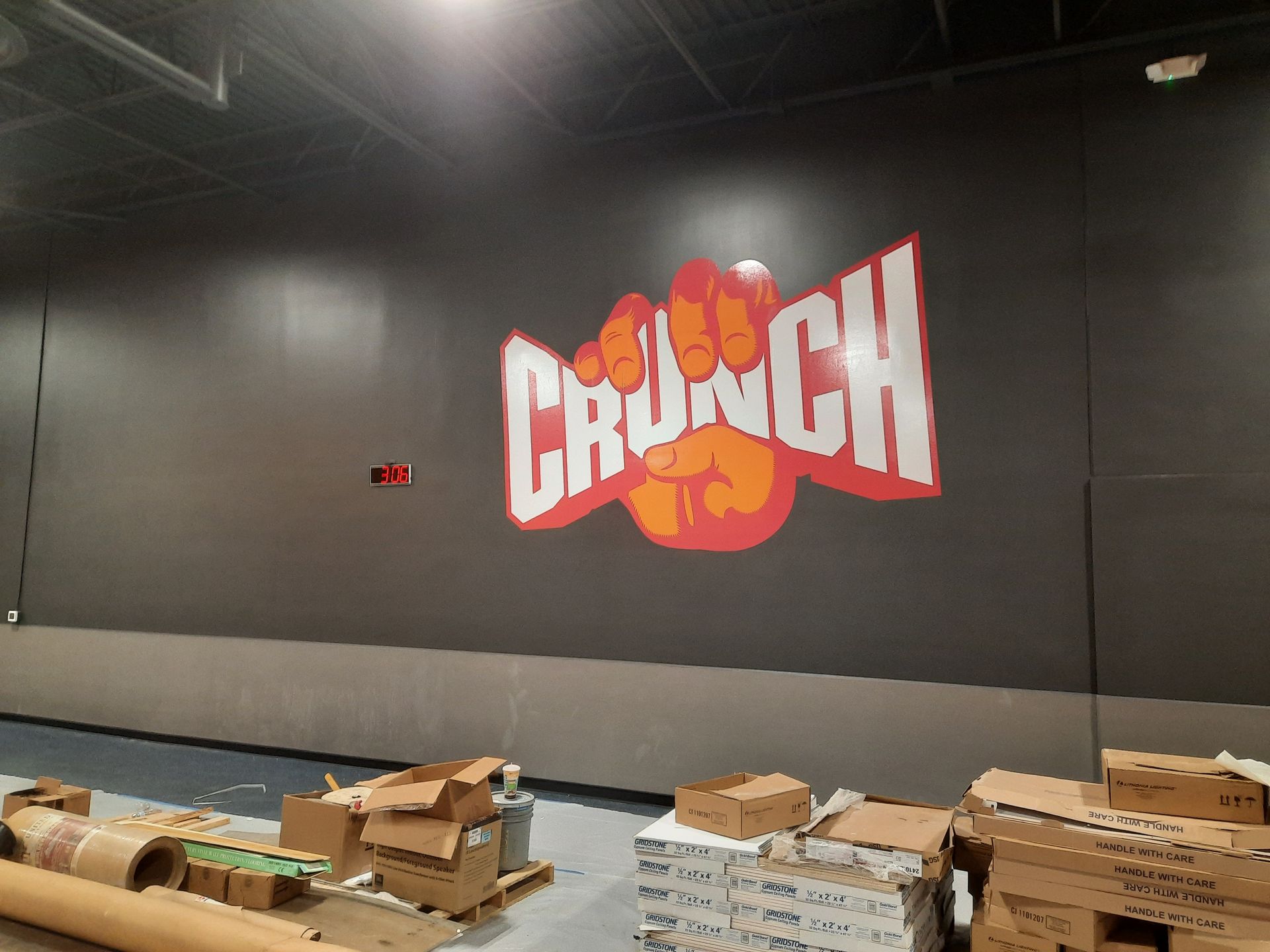 CRUNCH logo on a dark gym wall with boxes and supplies along the floor.