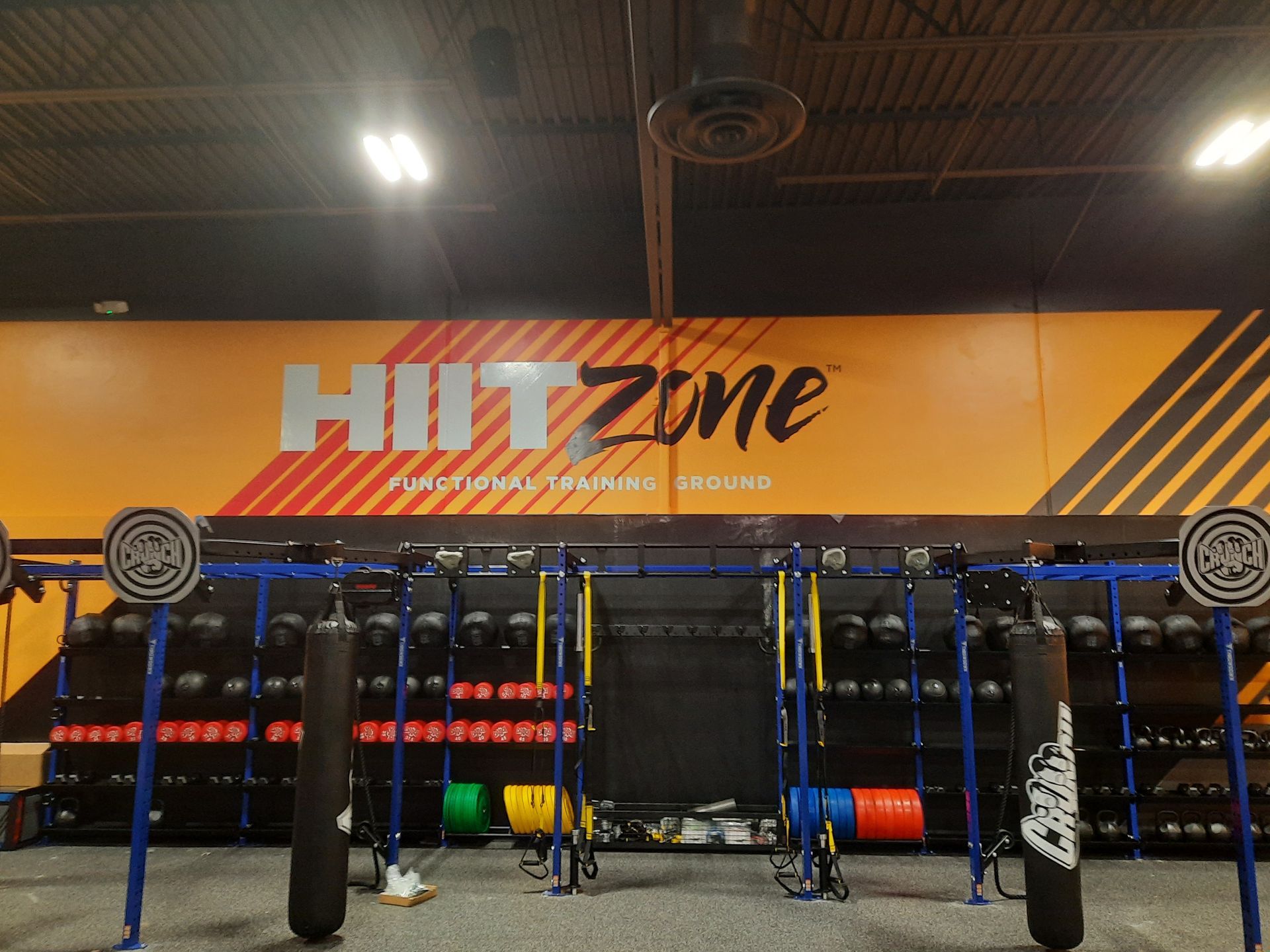 HIIT Zone gym with barbell racks, punching bag, and training equipment under orange wall signage