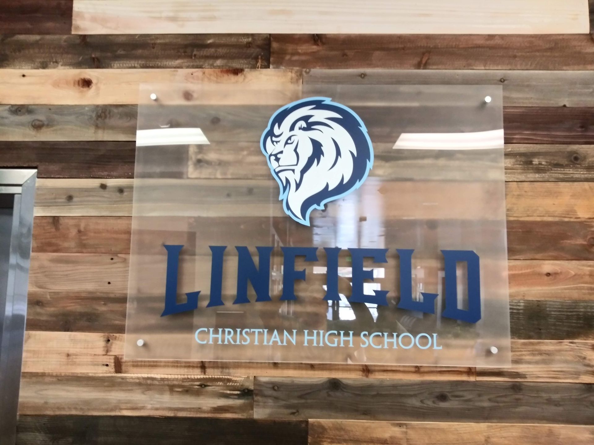 Wooden wall sign for Linfield Christian High School with blue lion logo and lettering