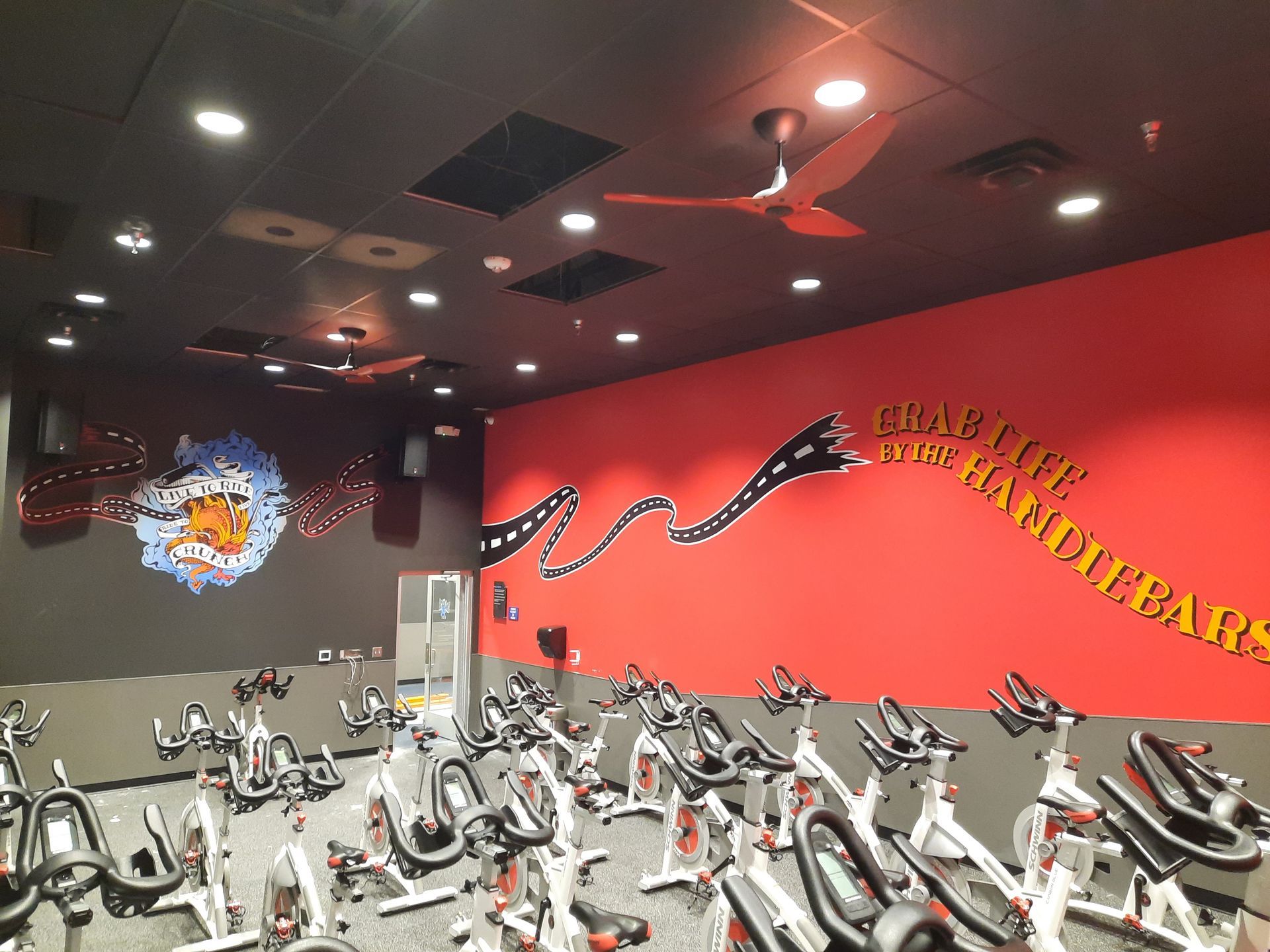 Indoor gym with rows of stationary bikes, red accent wall, and ceiling lights