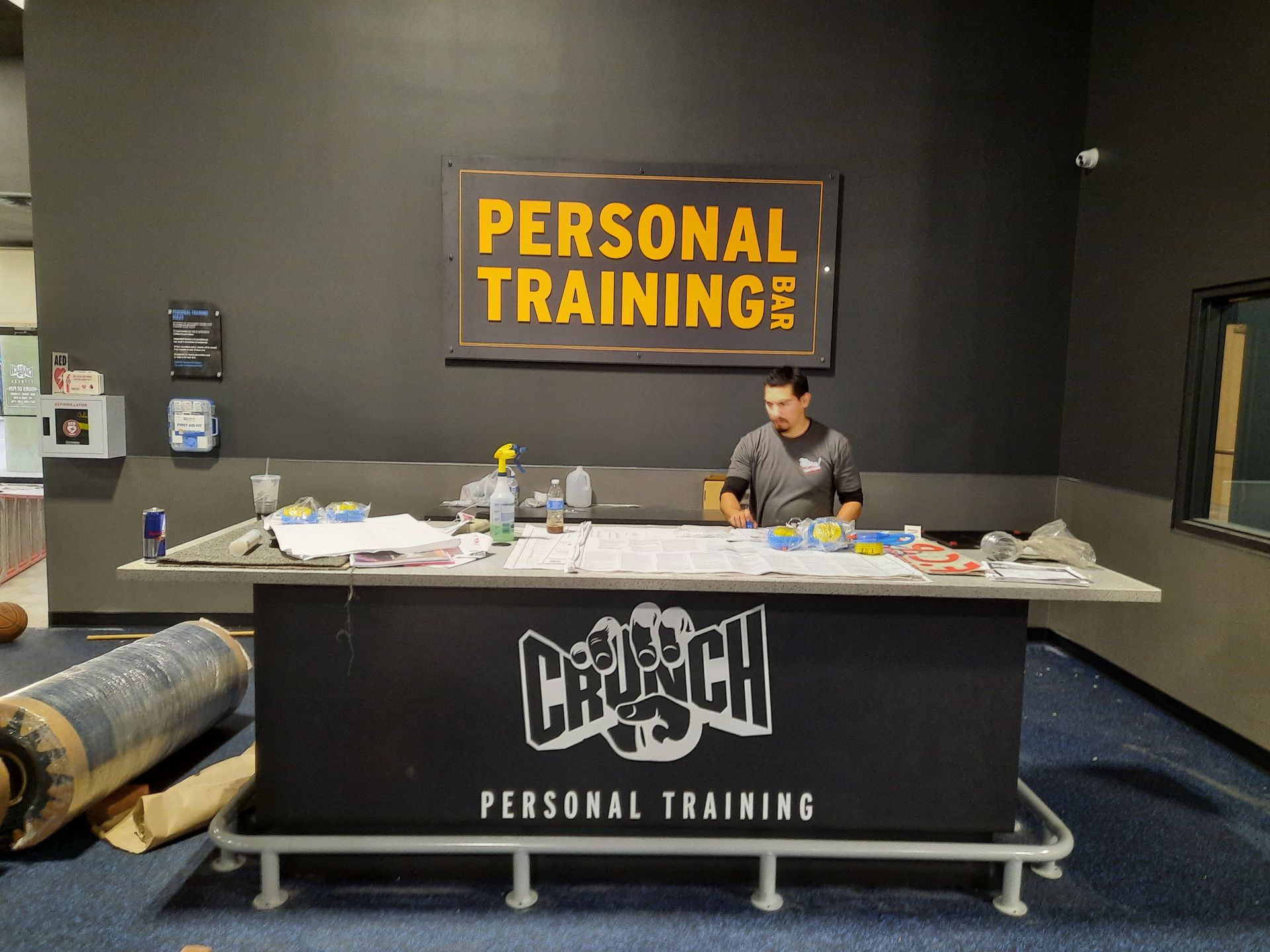 Personal training desk in a gym, with a staff member behind a counter under a “PERSONAL TRAINING” sign.