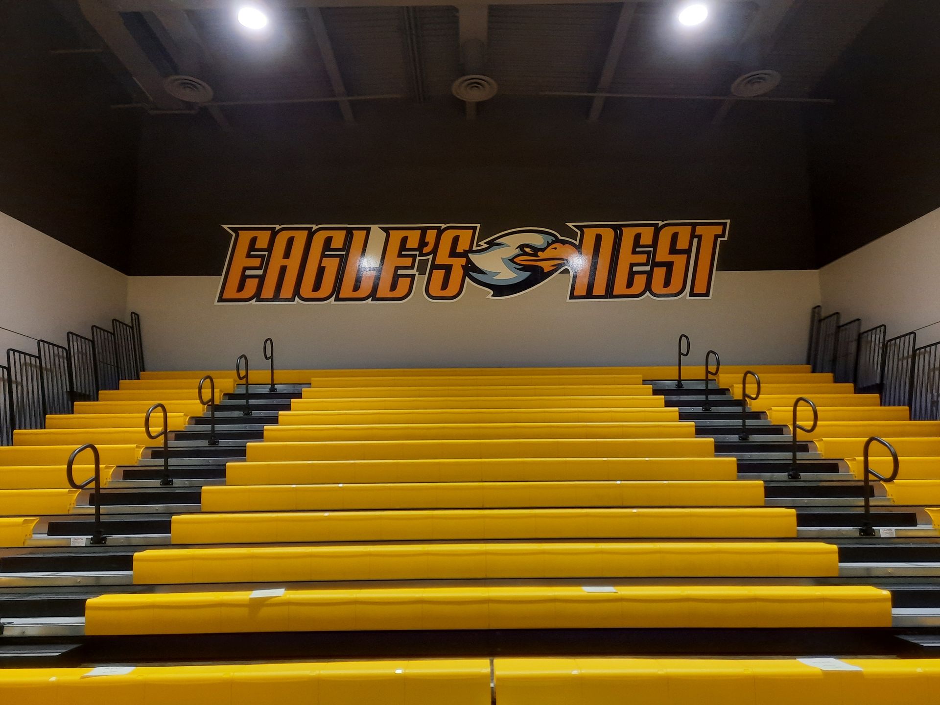 Empty gym bleachers with yellow seats and “Eagle’s Nest” mural on the wall