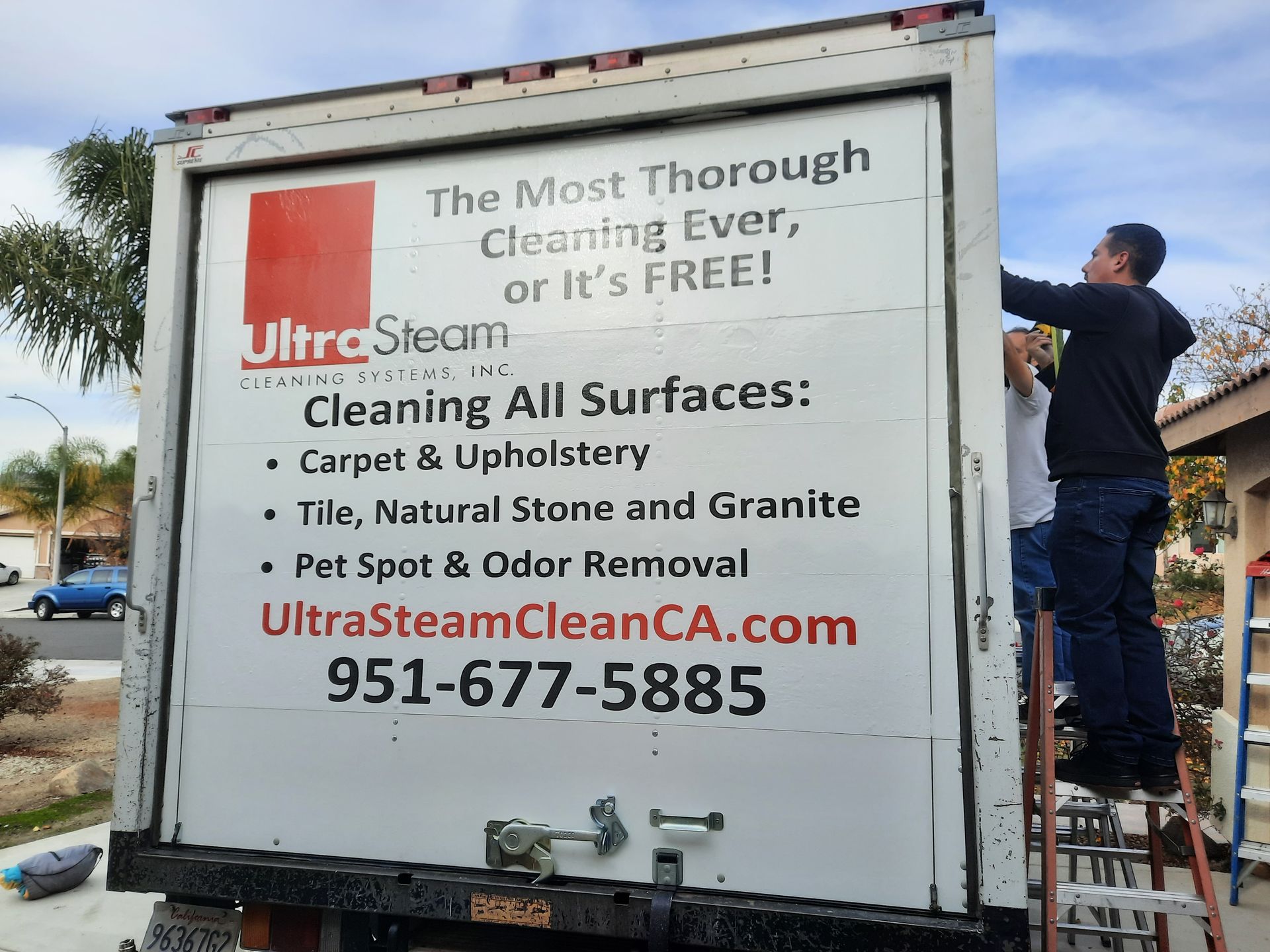 Worker on ladder installing a cleaning service sign on the back of a white truck