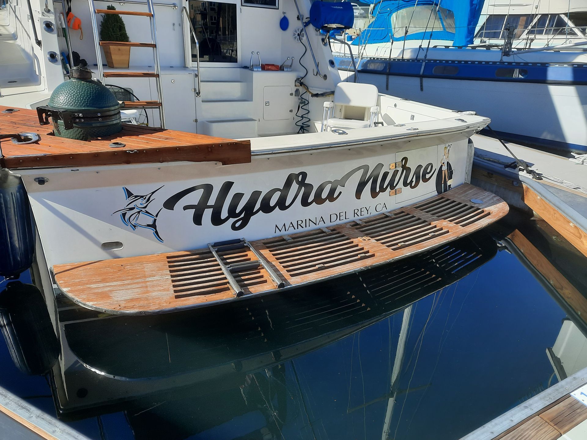 White yacht stern with “Hydra H…” lettering, docked beside blue water and another boat