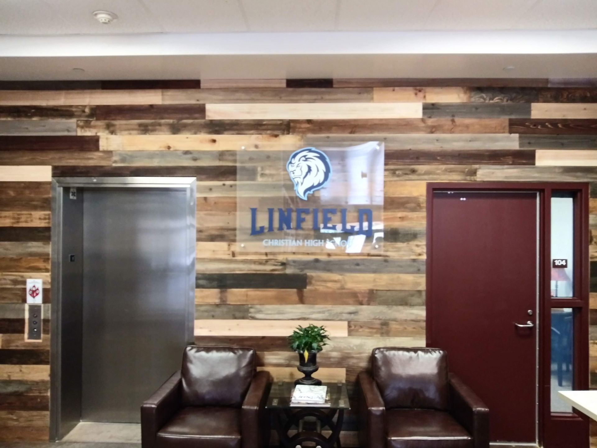 Lobby with wood-paneled wall, elevator, red door, and bench seating beneath a “LINEFX” sign.