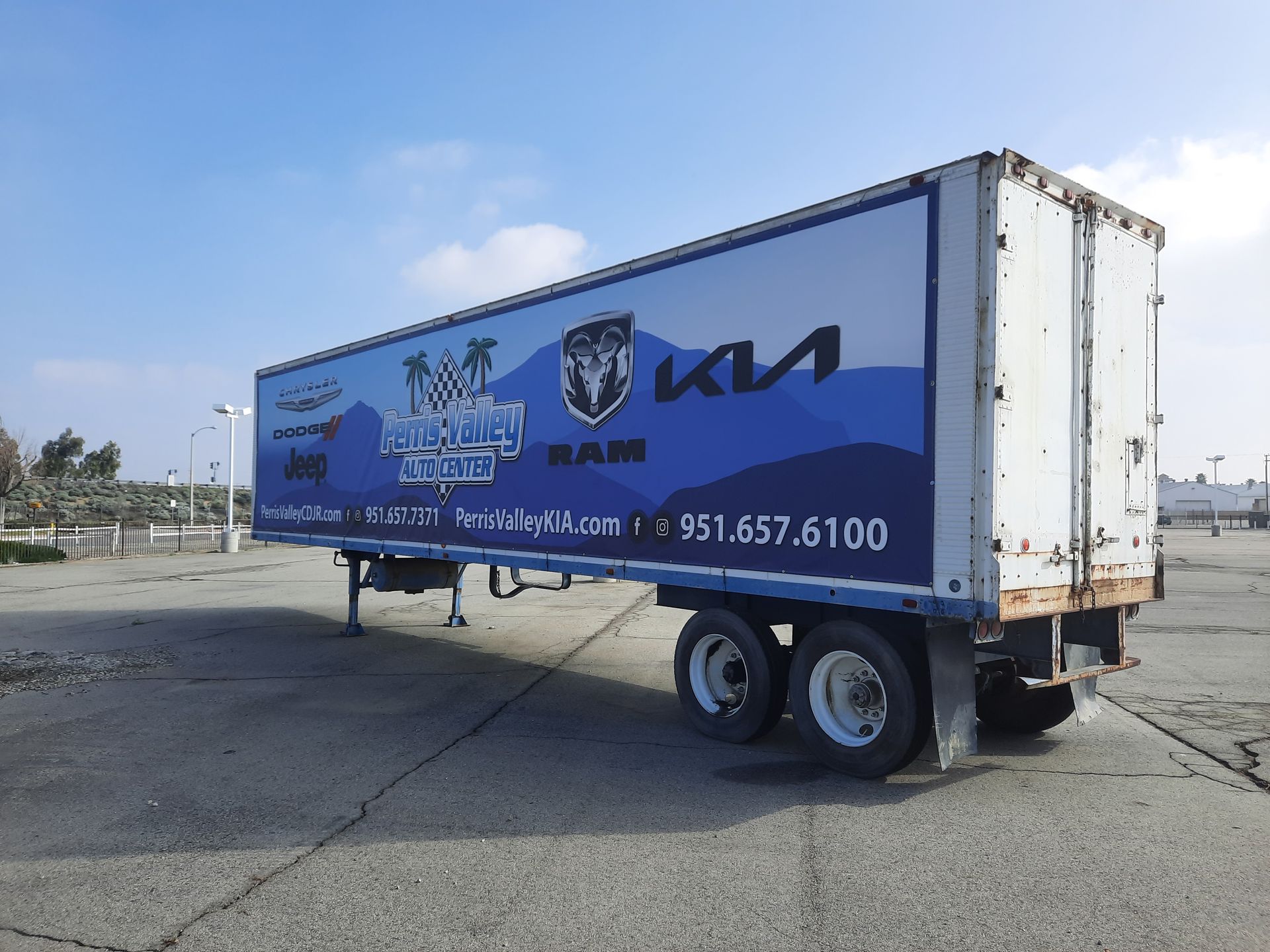 Blue Kia box truck parked on pavement under a clear sky, side view with company branding.