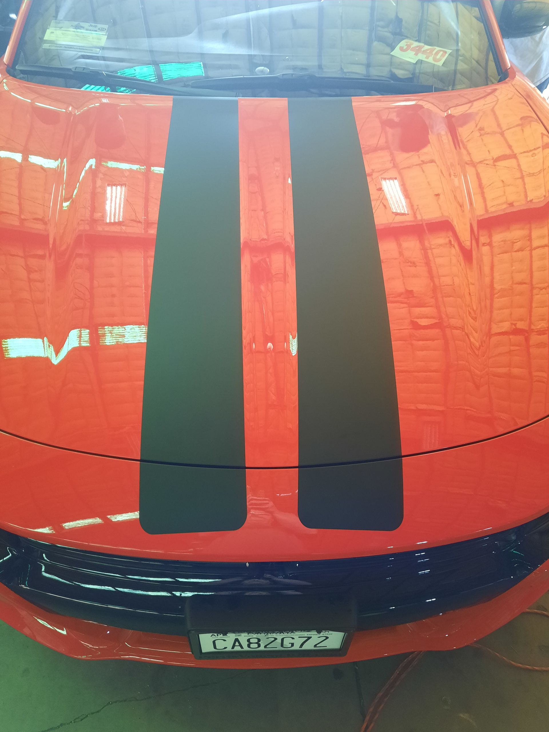 Front view of an orange sports car with two black racing stripes on the hood