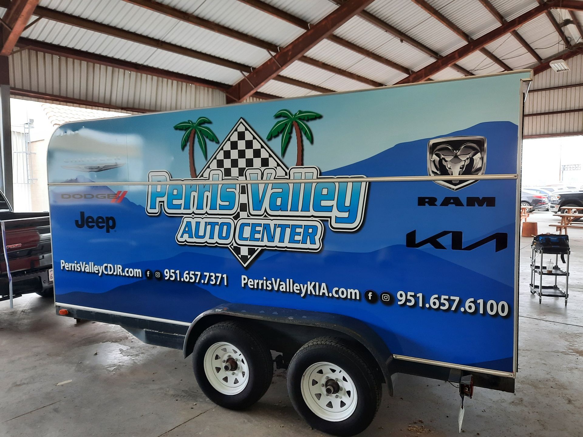 Blue Ferris Valley Auto Center trailer with Jeep, Ram and Kia logos under a covered structure