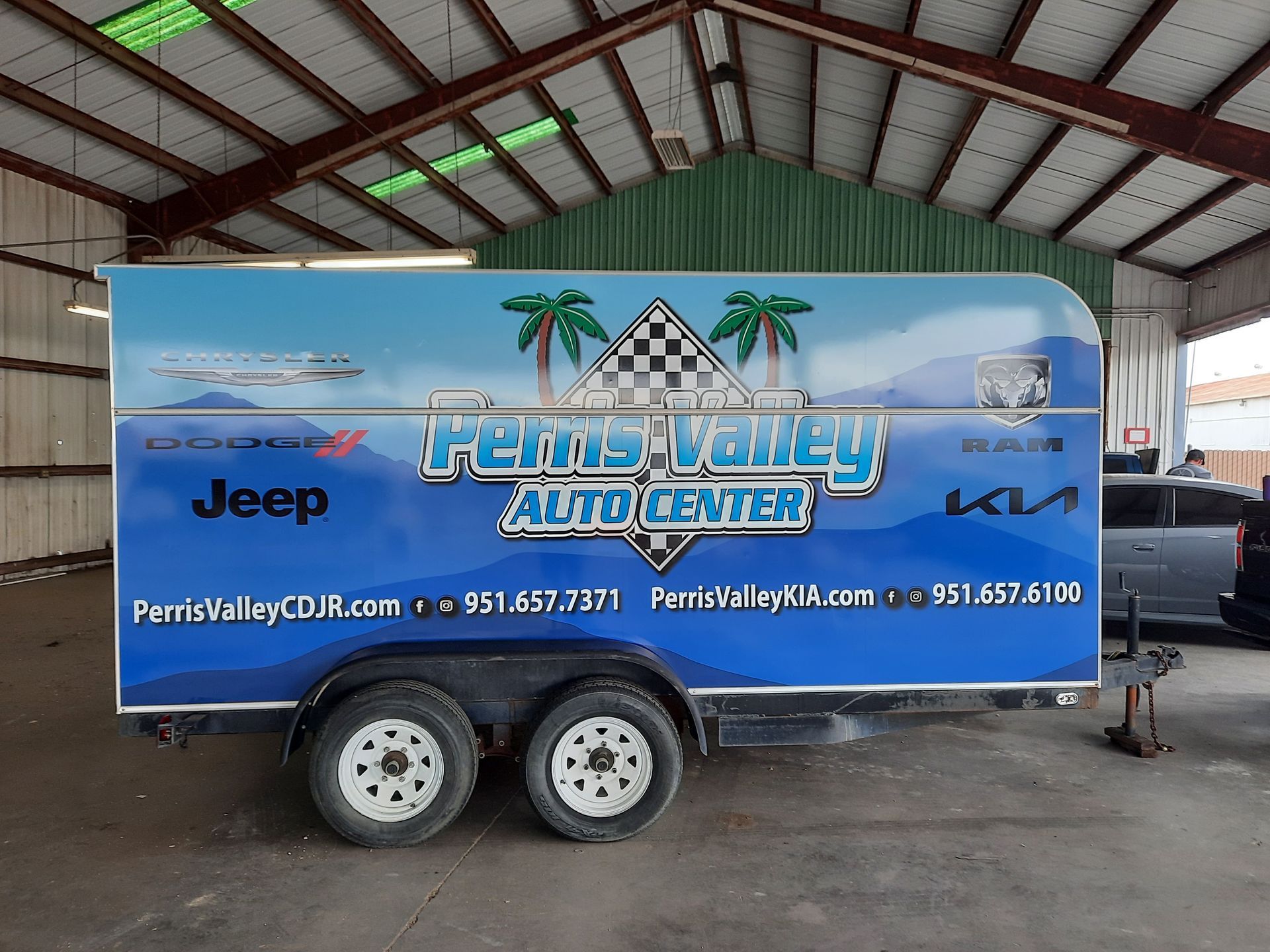 Blue trailer wrapped with Penins Valley Auto Center and Jeep/Kia logos inside a warehouse.