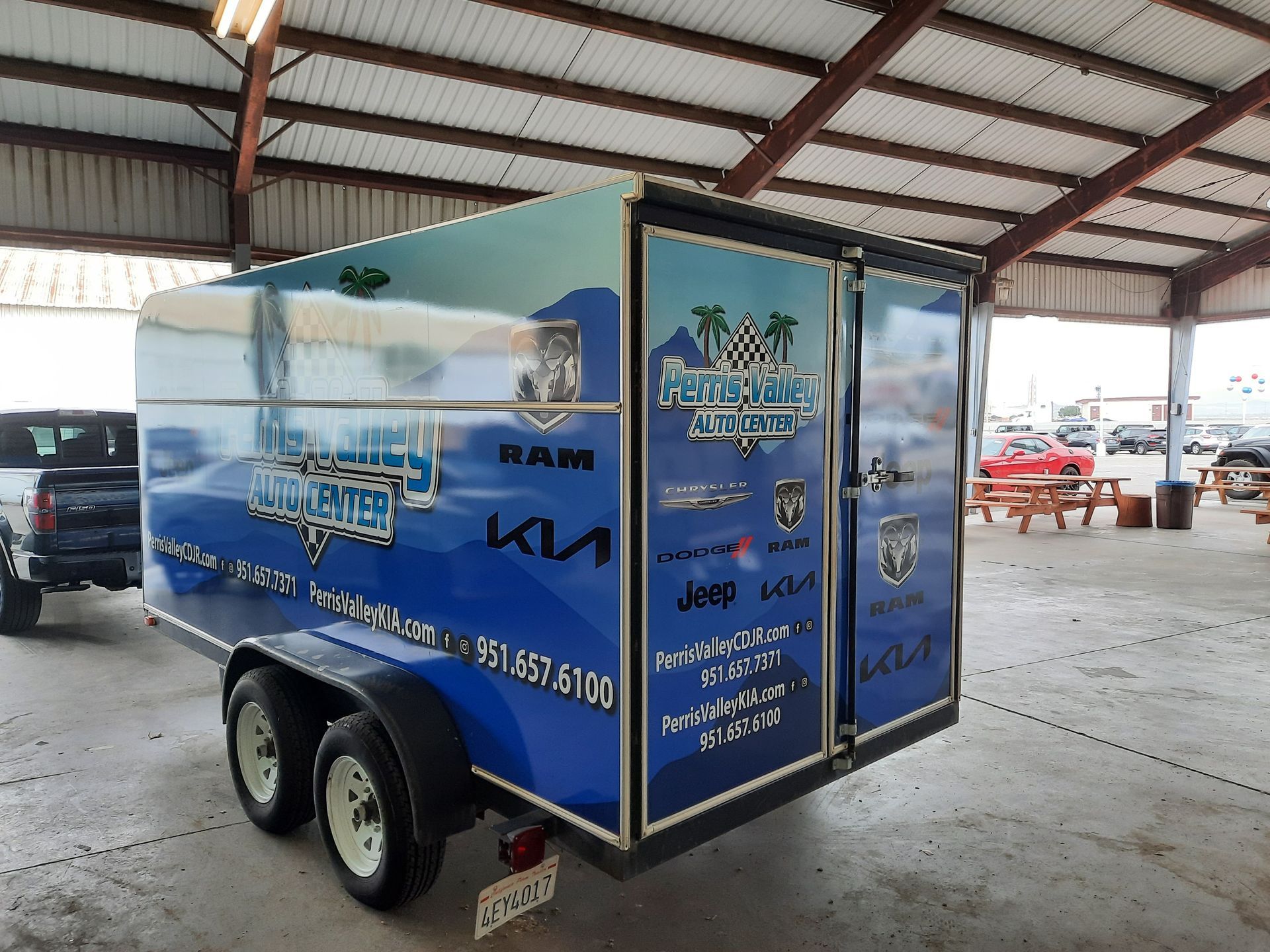 Blue Kia-branded enclosed trailer with mountain graphics parked inside a warehouse.